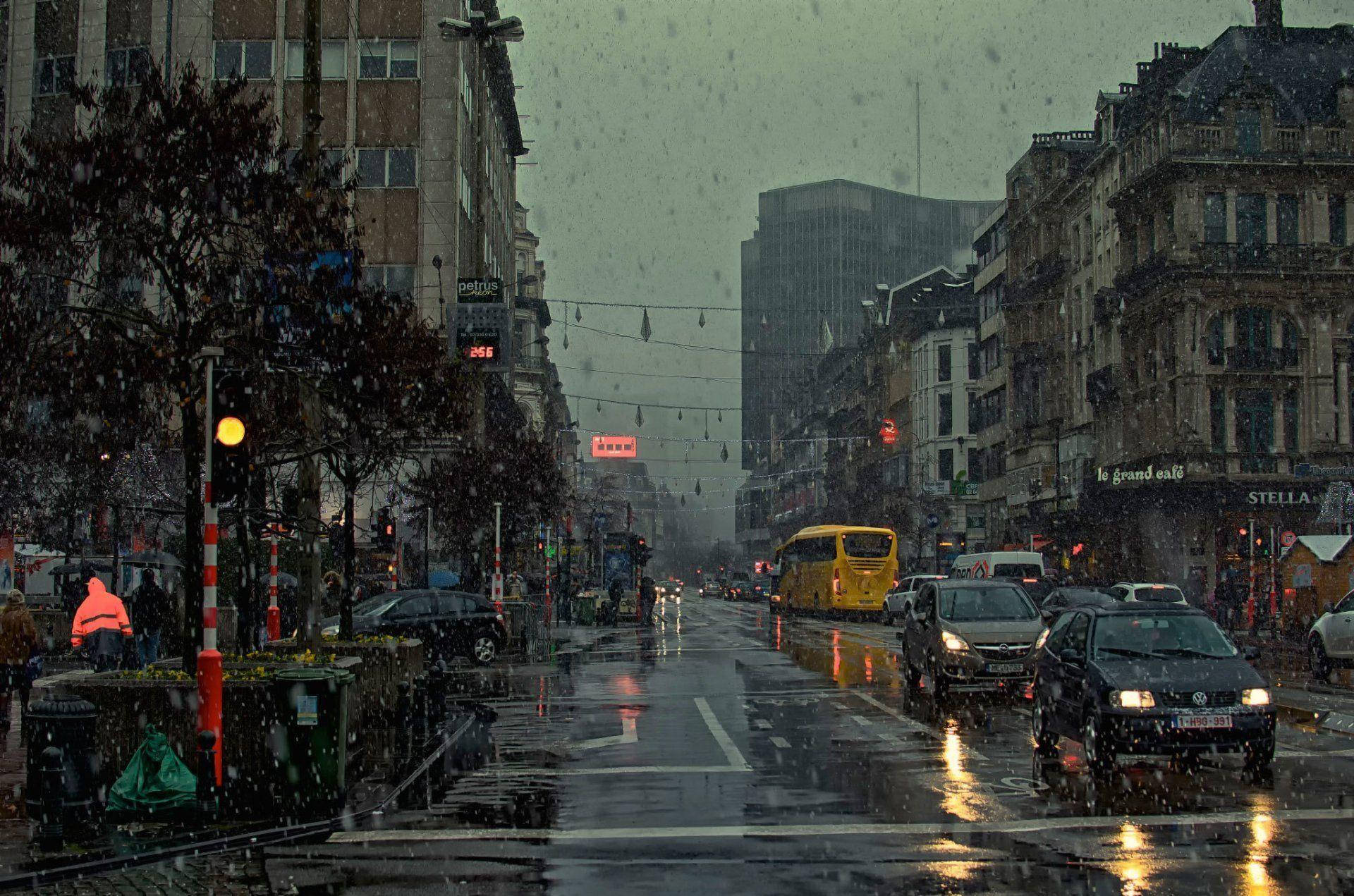 城市 桌布 壁紙 — 黃昏時分下雨的城市街道，濕漉漉的路面反射著車燈，一輛黃色巴士在車流中行駛。