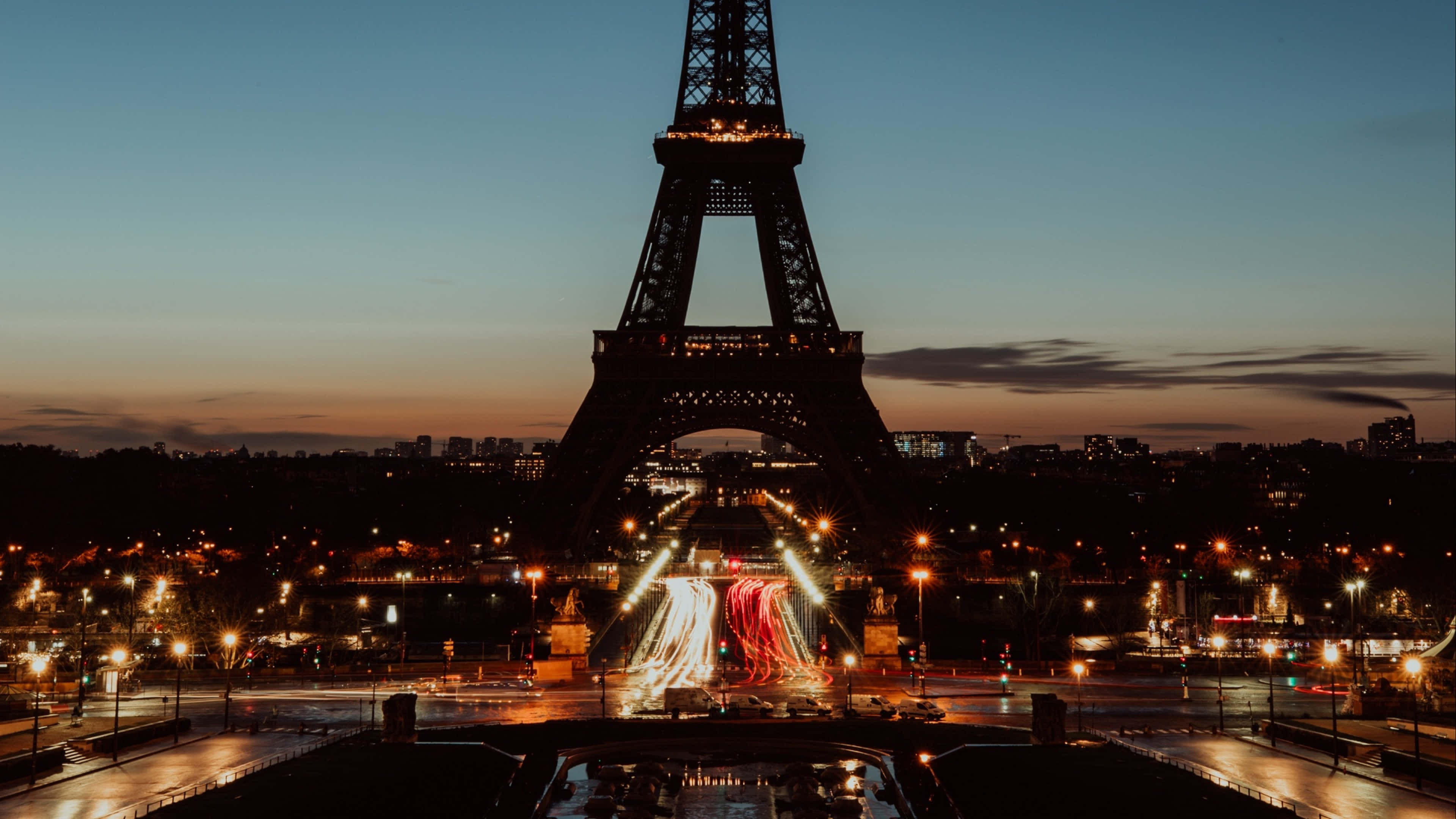 Paris At Night 桌布 壁紙 — 黃昏時分亮燈的艾菲爾鐵塔，前景有汽車燈光流動形成的線條。
