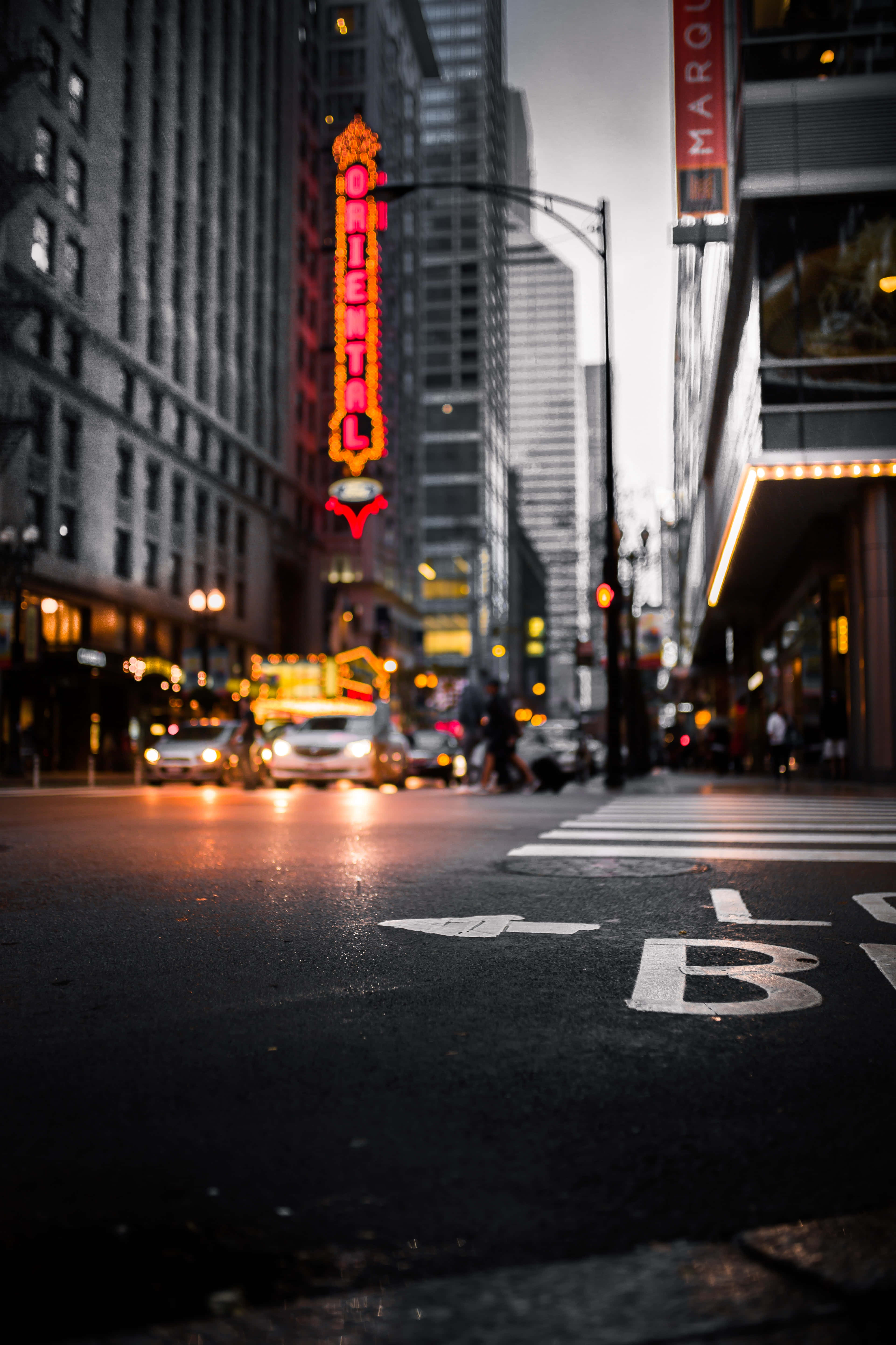 City Street 桌布 壁紙 — 黃昏時分低角度拍攝的城市街道，一個發光的紅色 'ORIENTAL' 霓虹燈牌聳立在模糊的汽車和行人之上。