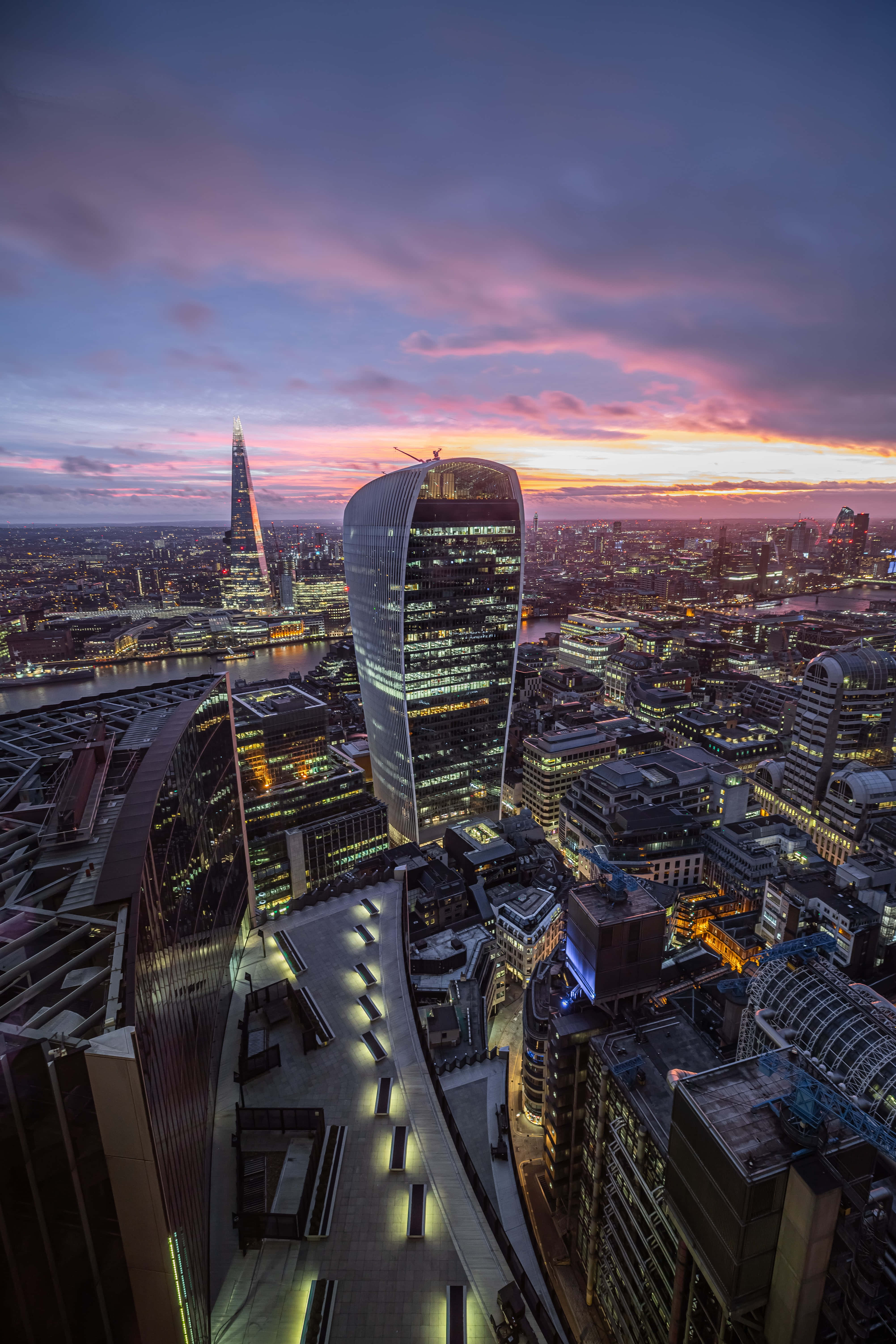 London iPhone 桌布 壁紙 — 黃昏時分倫敦天際線的鳥瞰圖，粉橙色天空照亮現代摩天大樓和下方的河流。