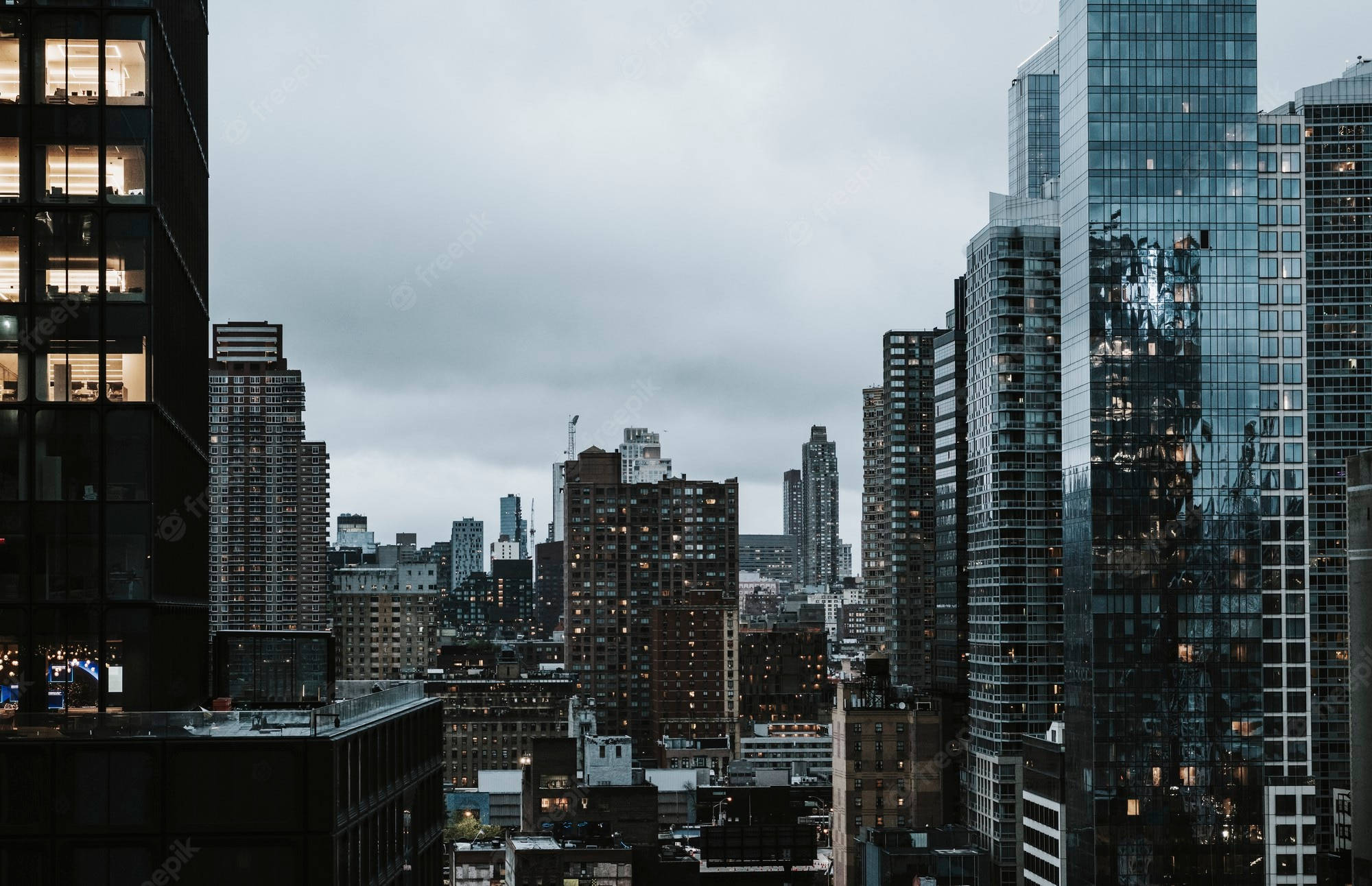 Buildings 桌布 壁紙 — 黃昏時分充滿氛圍的城市天際線，高聳的玻璃摩天大樓映照著多雲的天空和發光的窗戶。