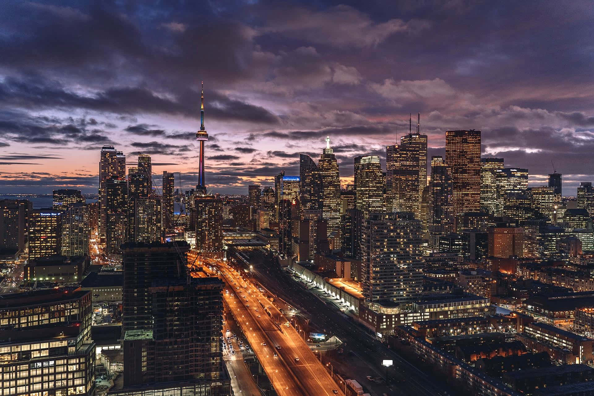 Toronto Skyline 桌布 壁紙 — 黃昏時分充滿活力的城市天際線，摩天大樓燈火通明，CN塔在戲劇性的紫色和橙色天空下閃閃發光。