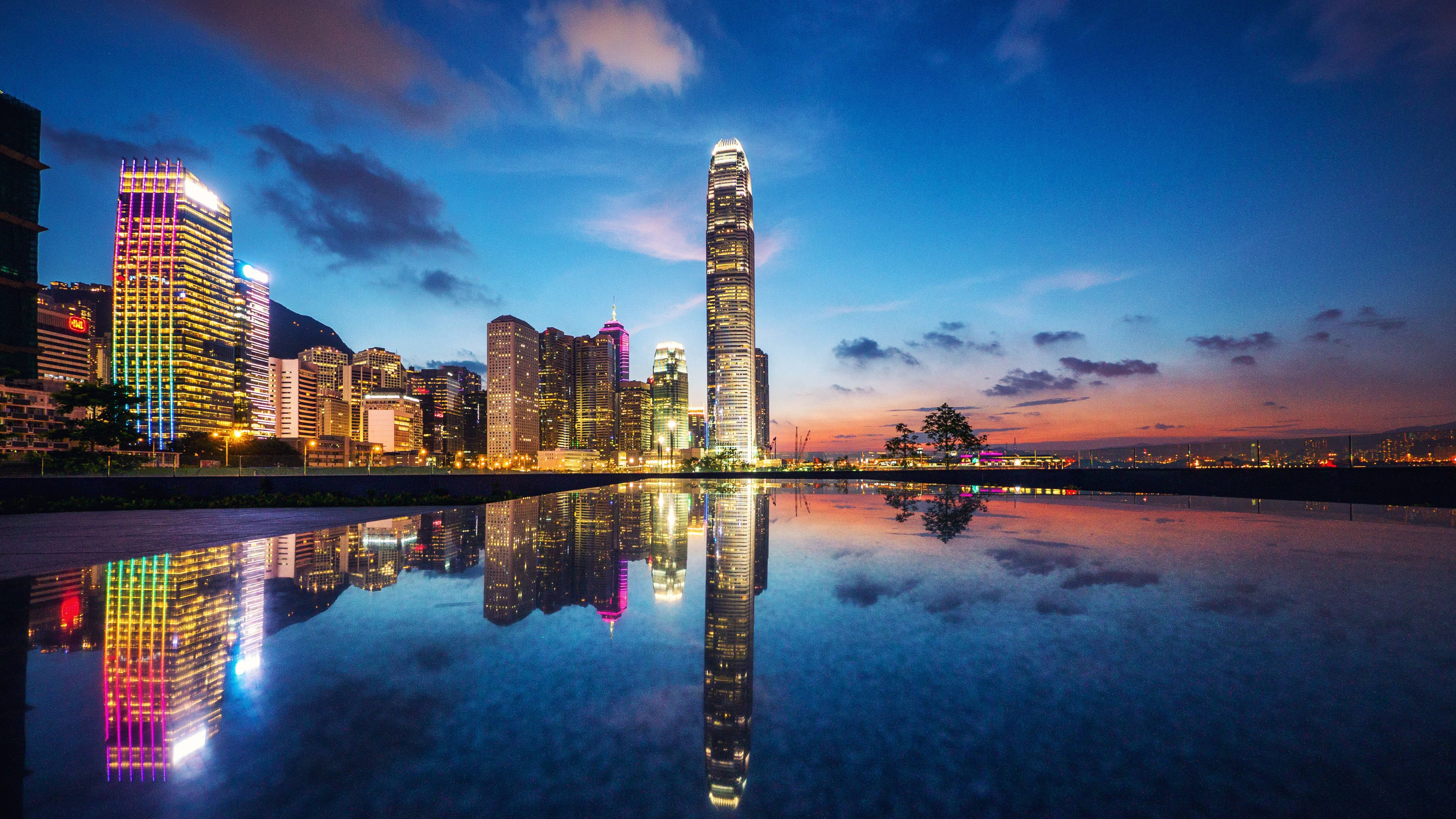 Architecture 桌布 壁紙 — 黃昏時分充滿活力的城市天際線，摩天大樓在漸變天空下倒映在平靜的水面上。