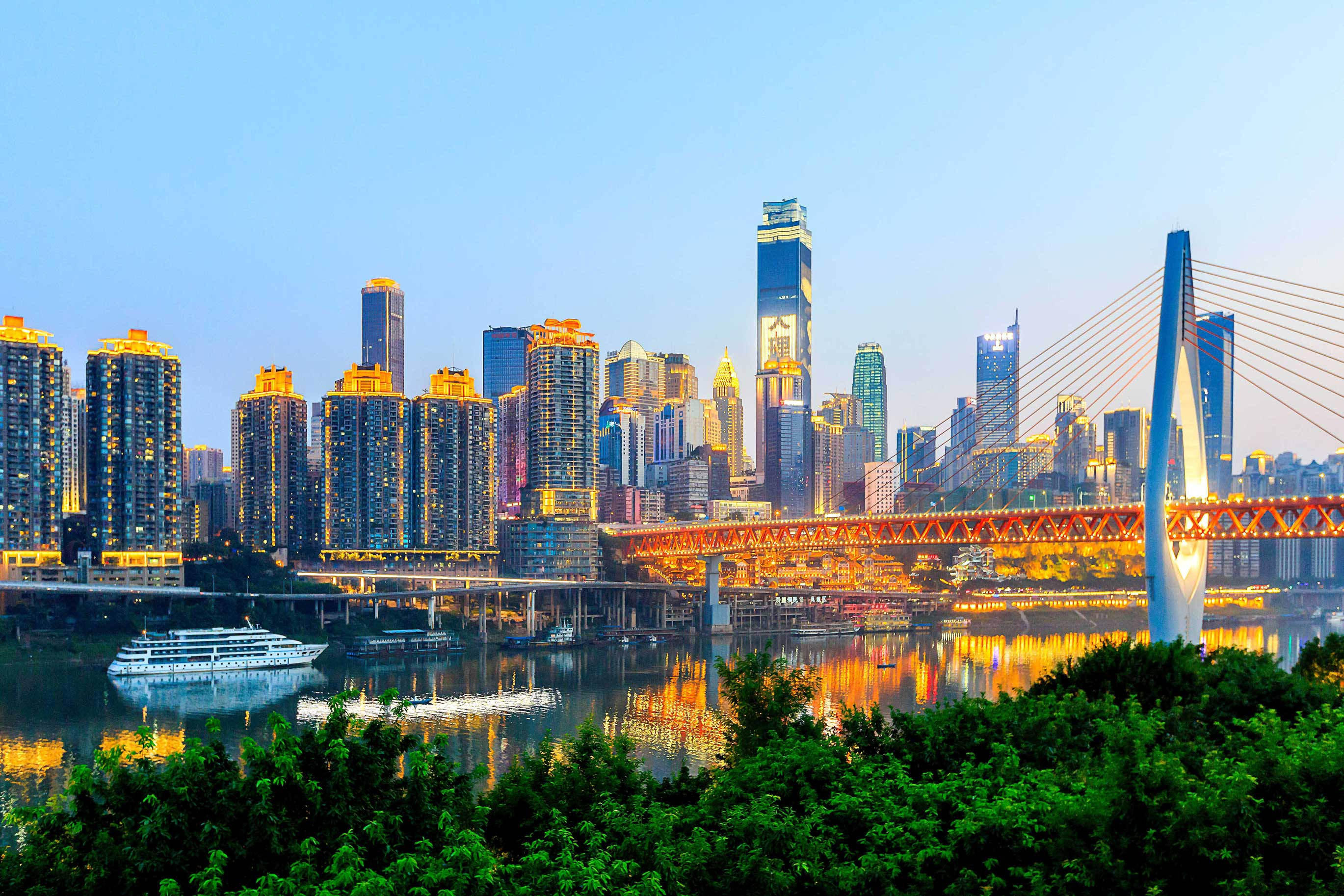 Harbin 桌布 壁紙 — 黃昏時分充滿活力的城市天際線，明亮的摩天大樓和發光的橋樑倒映在平靜的水面上。