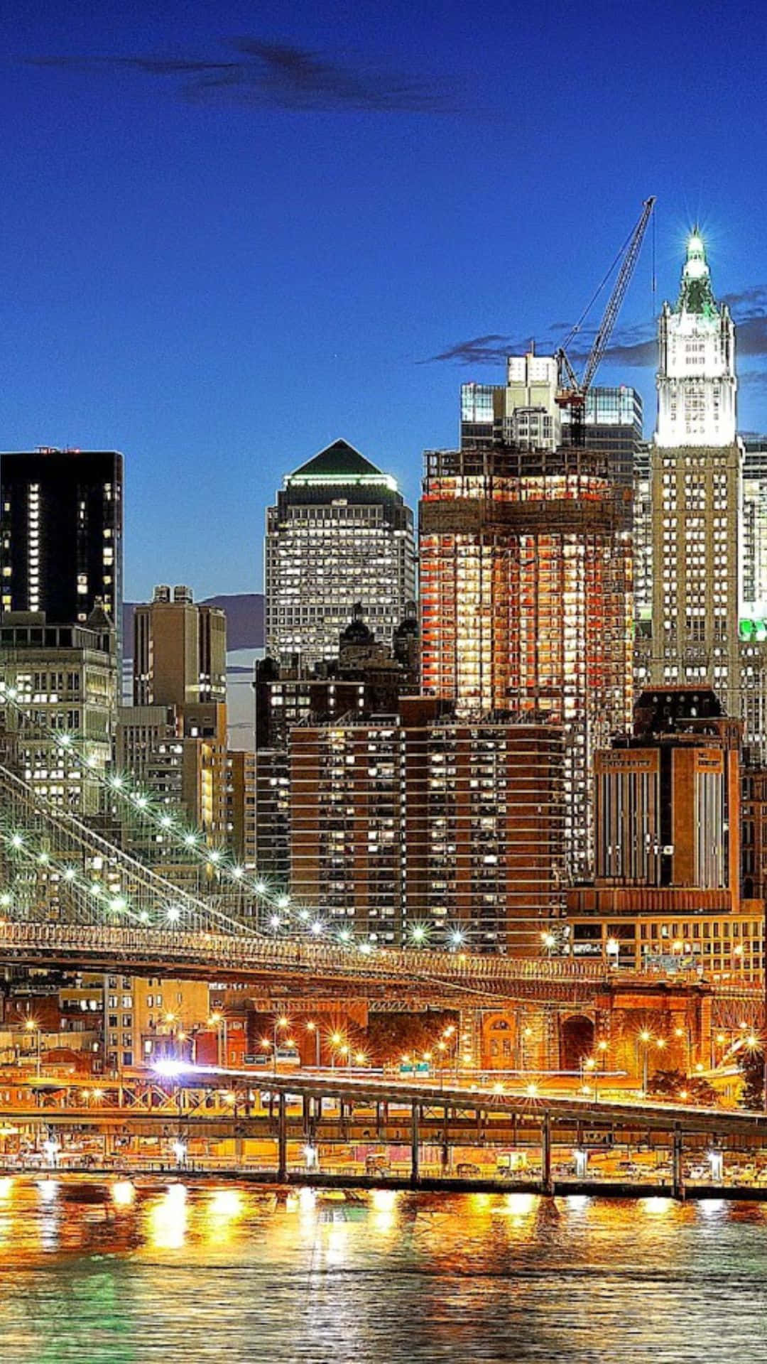 Android Ny City 桌布 壁紙 — 黃昏時分充滿活力的城市天際線，燈火通明的摩天大樓和發光的橋樑倒映在下面的水中。