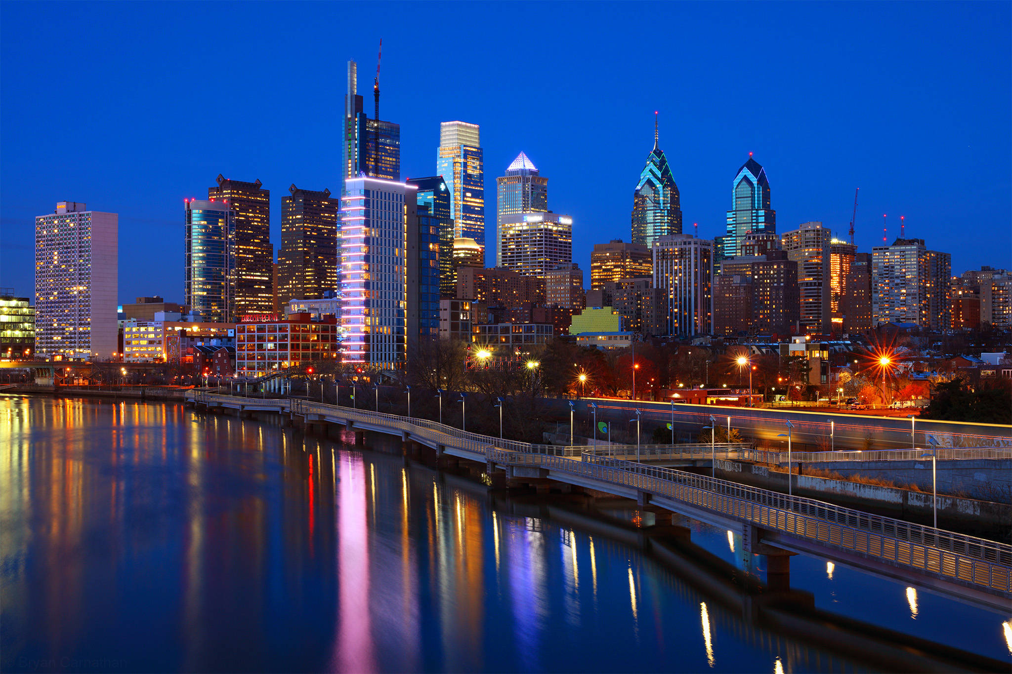 Philadelphia 桌布 壁紙 — 黃昏時分充滿活力的城市天際線，燈火通明的摩天大樓倒映在下方平靜的水面上。