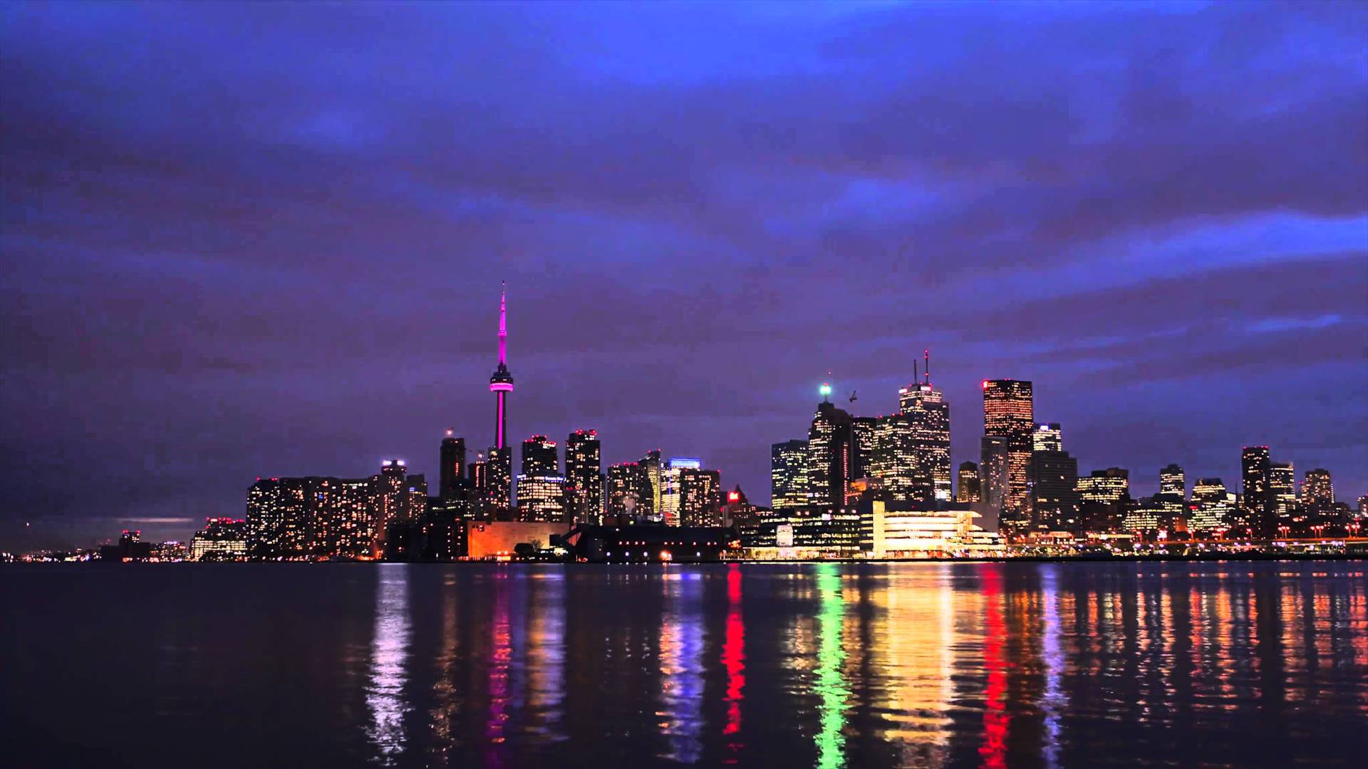 Toronto 桌布 壁紙 — 黃昏時分充滿活力的城市天際線，燈火通明的摩天大樓和閃爍的CN塔倒映在平靜的水面上。