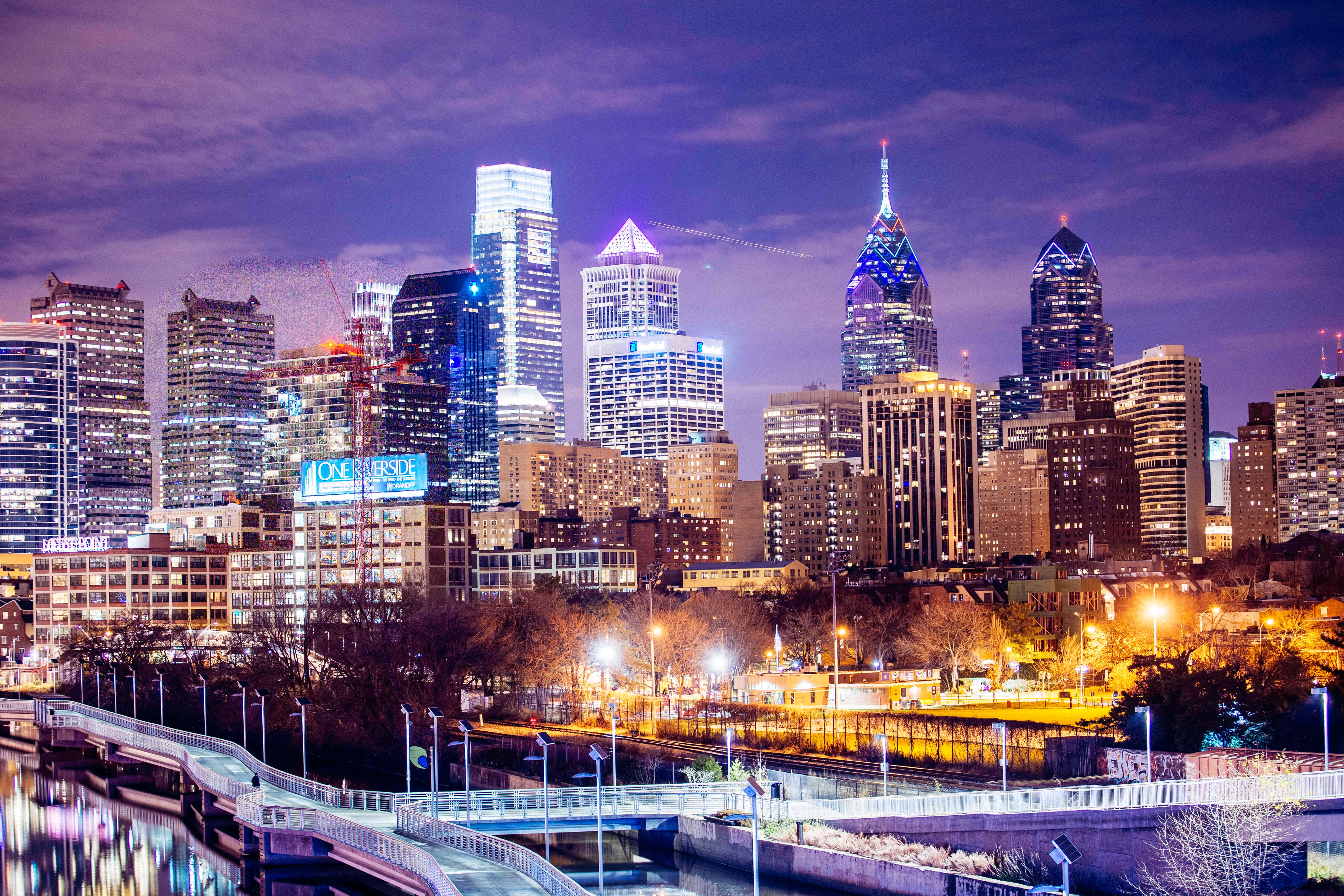 Philly 桌布 壁紙 — 黃昏時分充滿活力的城市天際線，燈火通明的摩天大樓倒映在下面的河流中。