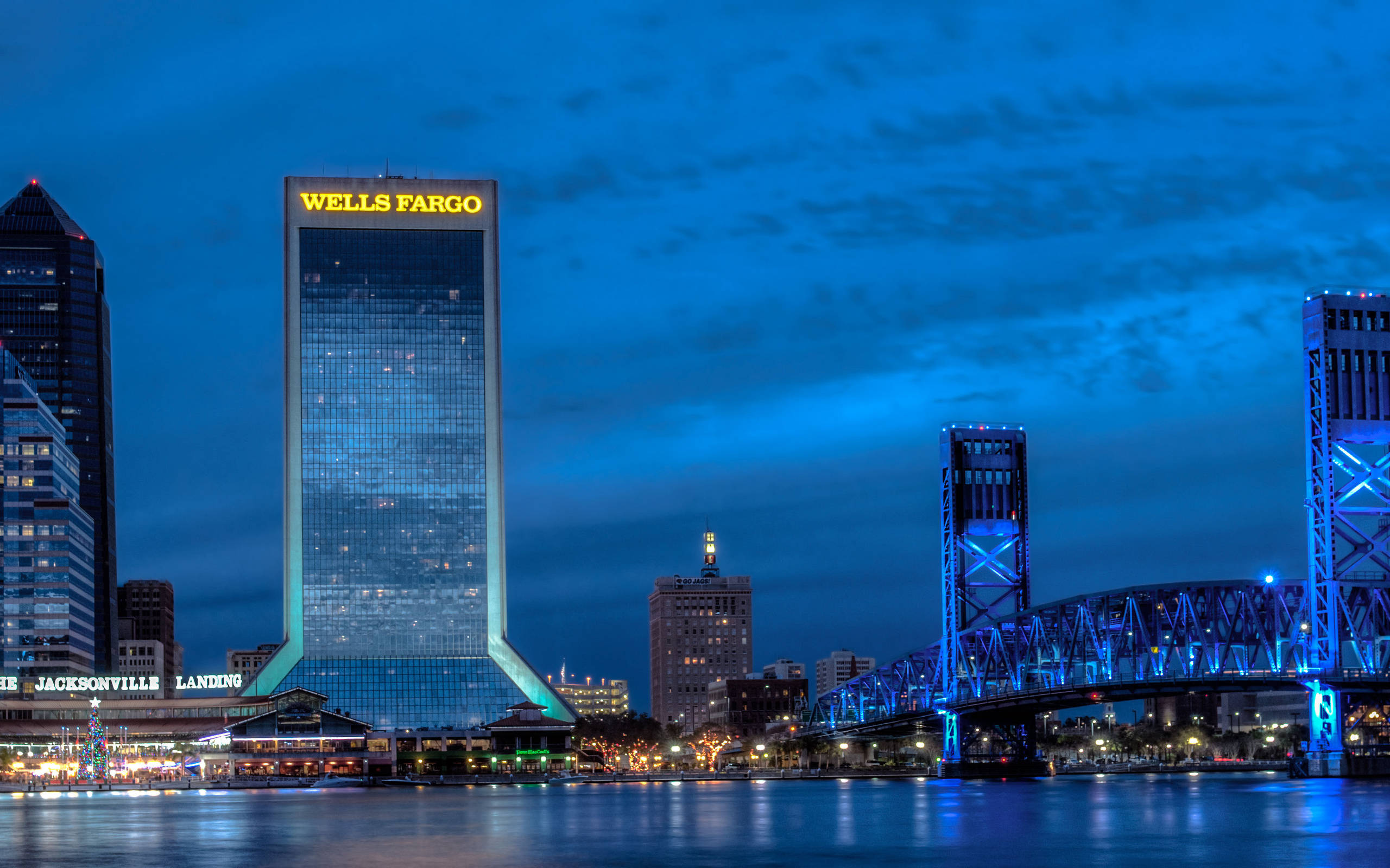 夜空 桌布 壁紙 — 黃昏時分充滿活力的城市天際線，發光的 Wells Fargo 塔和藍色燈光的橋樑倒映在平靜的水面上。