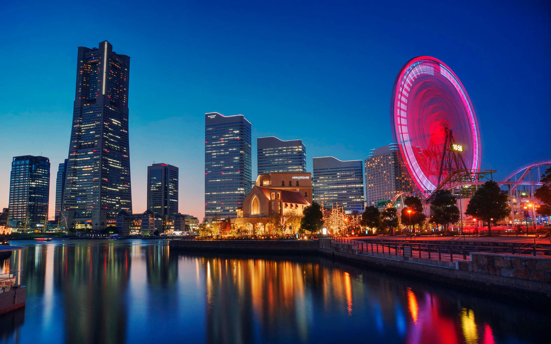 Yokohama 桌布 壁紙 — 黃昏時分充滿活力的城市天際線，發光的粉紅色摩天輪倒映在平靜的水面上。
