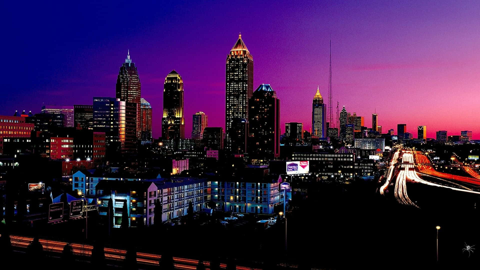 夜景城市 桌布 壁紙 — 黃昏時分充滿活力的城市天際線，紫色和粉紅色的天空，摩天大樓和流動交通的閃爍燈光。