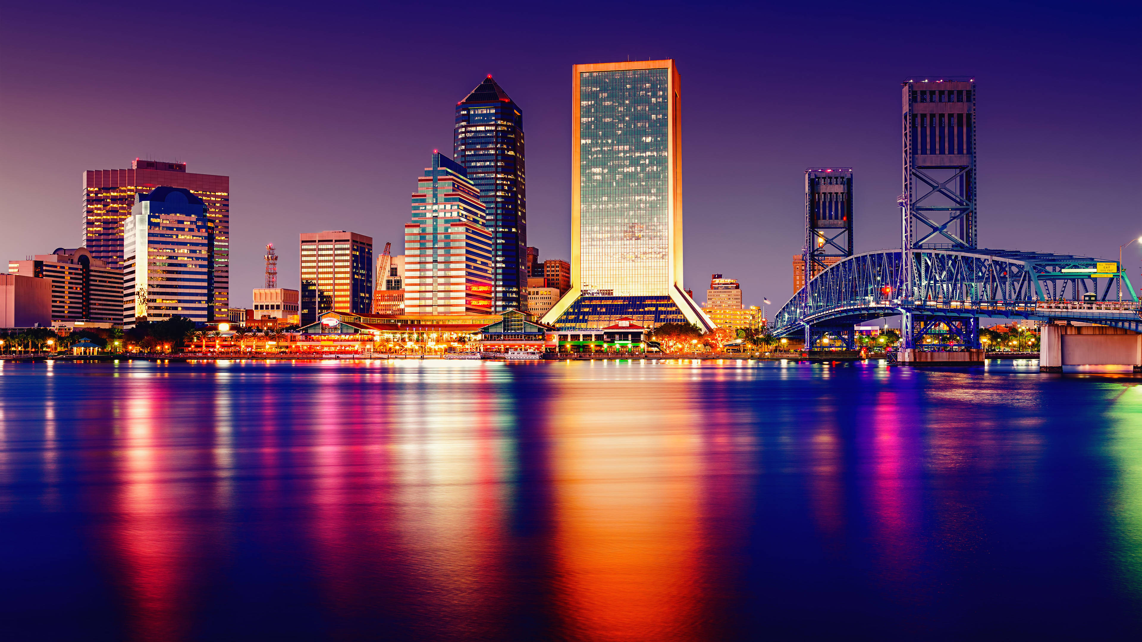 florida 桌布 壁紙 — 黃昏時分充滿活力的城市天際線，閃爍的摩天大樓和橋樑倒映在平靜的水面上。