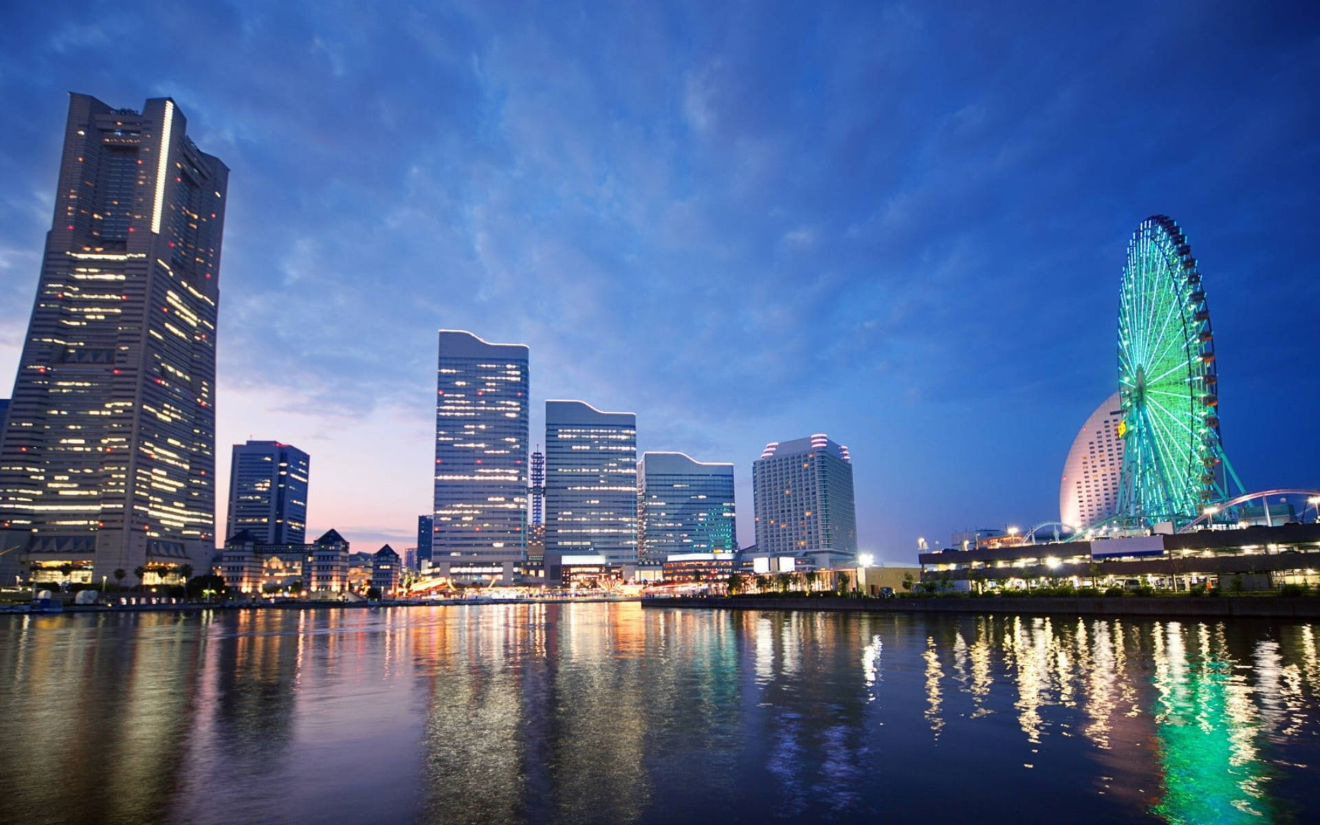 Yokohama 桌布 壁紙 — 黃昏時分充滿活力的城市天際線，閃爍的摩天大樓和霓虹燈摩天輪倒映在平靜的水面上。