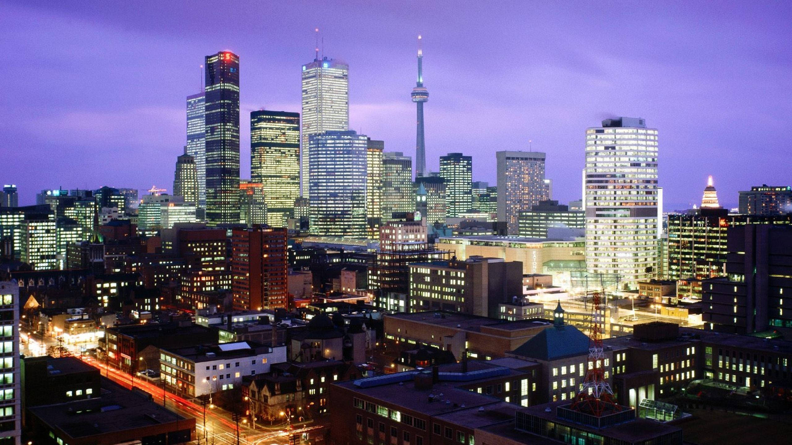 Toronto 桌布 壁紙 — 黃昏時分充滿活力的城市天際線，閃爍的摩天大樓和標誌性的CN塔映襯著紫色的天空。