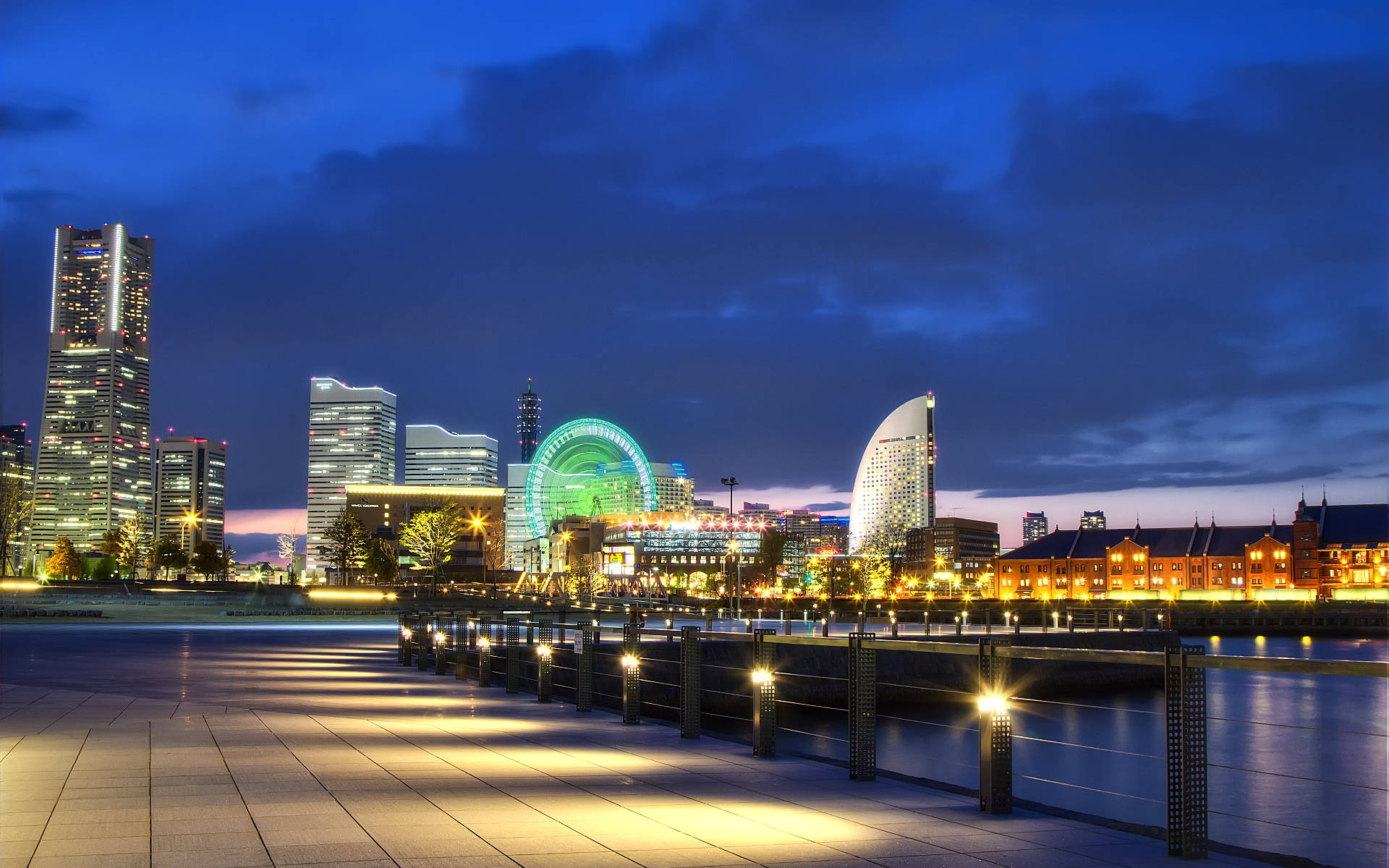 Yokohama 桌布 壁紙 — 黃昏時分充滿活力的城市天際線，閃爍的摩天大樓和明亮的綠色摩天輪倒映在平靜的水面上。