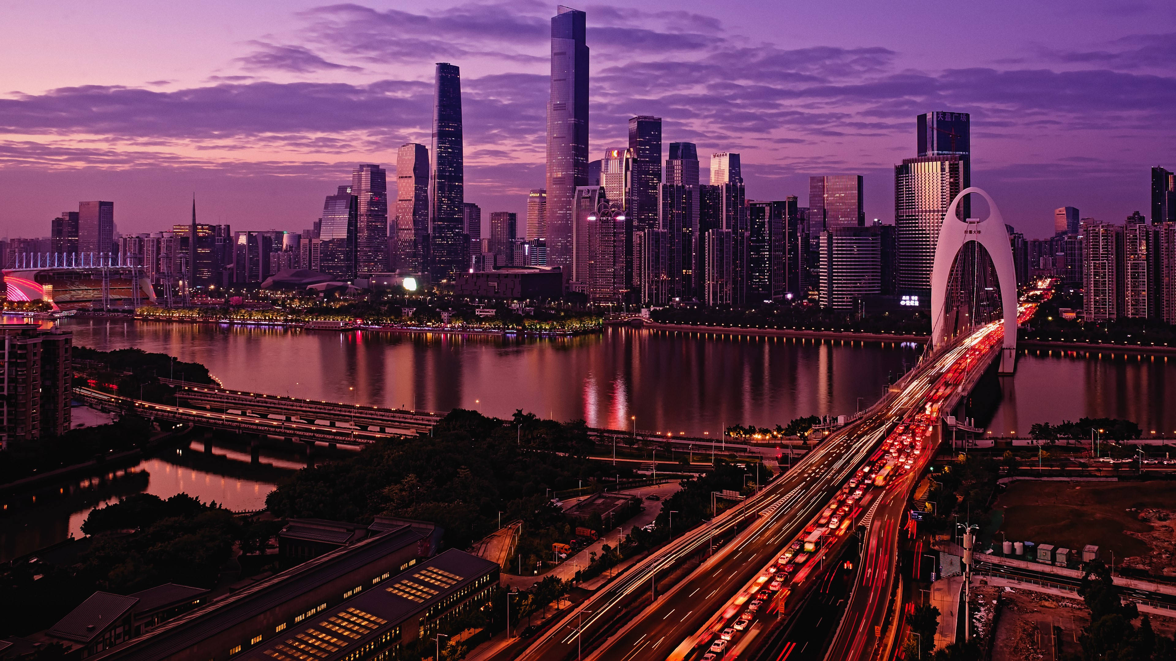 Chongqing 桌布 壁紙 — 黃昏時分充滿活力的城市天際線，閃爍的摩天大樓和河流反射出紫色和橙色的色調，車流沿著燈火通明的橋樑流動。