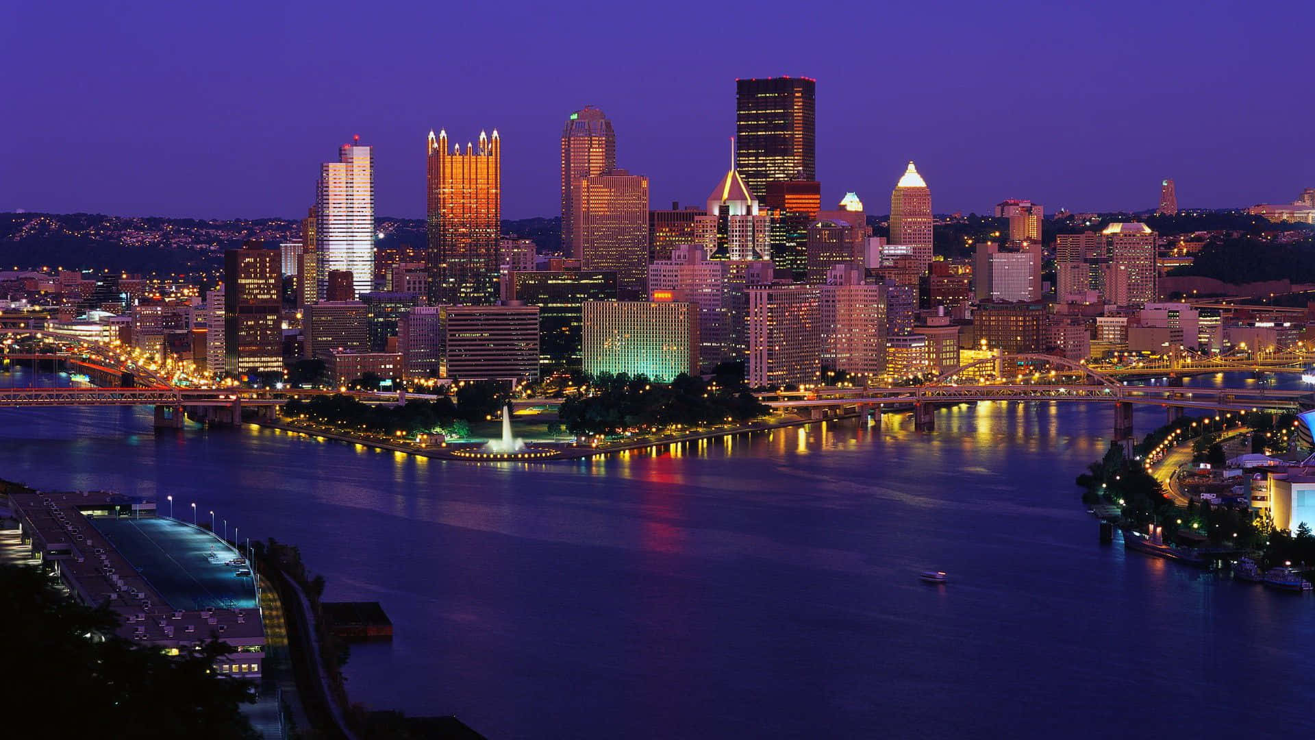 Pittsburgh Skyline 桌布 壁紙 — 黃昏時分充滿活力的城市天際線，閃爍的摩天大樓倒映在下面的河流中。