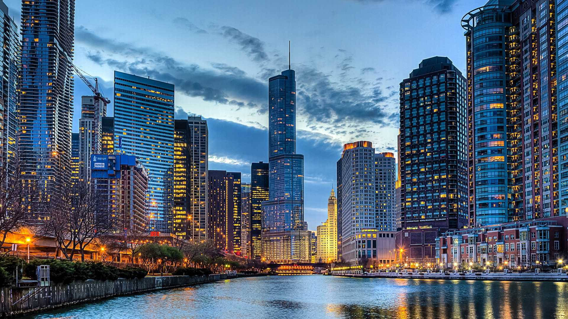 Skyscraper 桌布 壁紙 — 黃昏時分充滿活力的城市天際線，高聳的摩天大樓在下方平靜的河面上反射出溫暖的燈光。