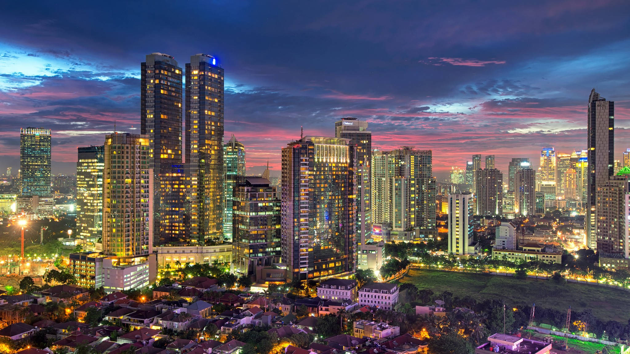 Jakarta 桌布 壁紙 — 黃昏時分充滿活力的城市天際線，高聳的摩天大樓在戲劇性的紫色和橙色天空下閃耀。
