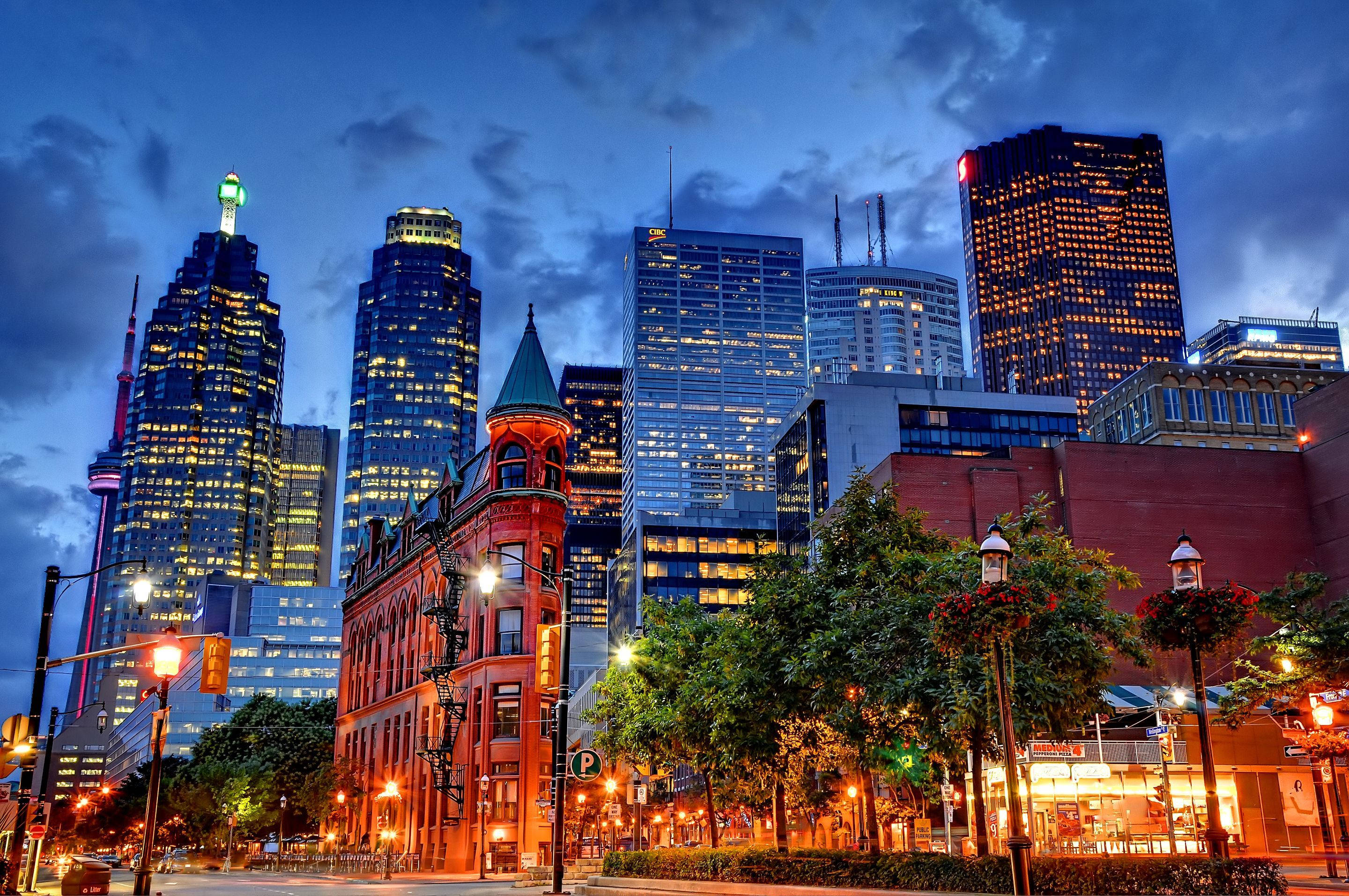 Toronto 桌布 壁紙 — 黃昏時分充滿活力的城市景觀，在憂鬱的藍天下，摩天大樓燈火通明，歷史悠久的紅磚建築矗立其中。