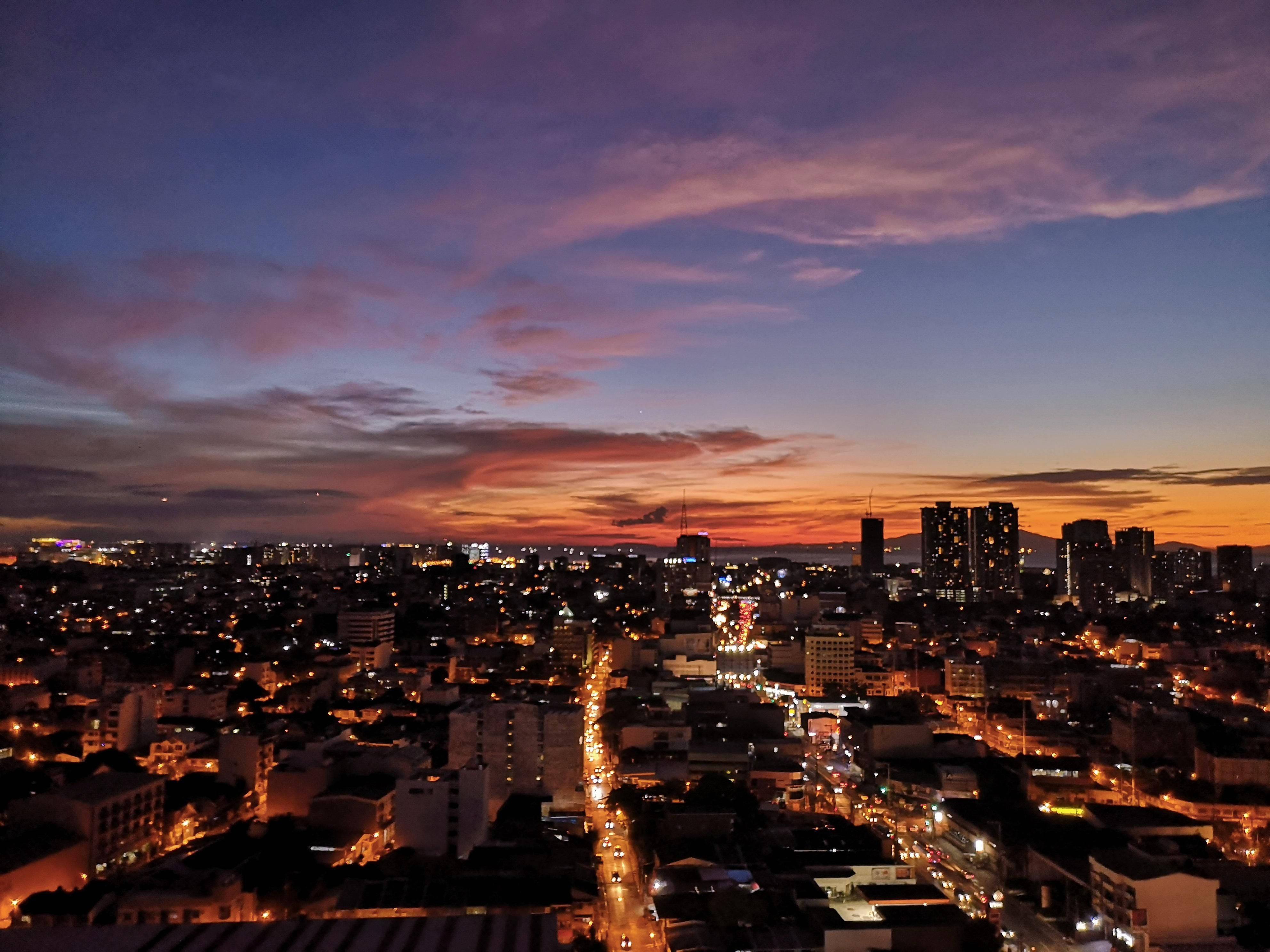 Manila 桌布 壁紙 — 黃昏時分充滿活力的城市景觀，在紫橙色天空下閃爍的街燈和建築物。