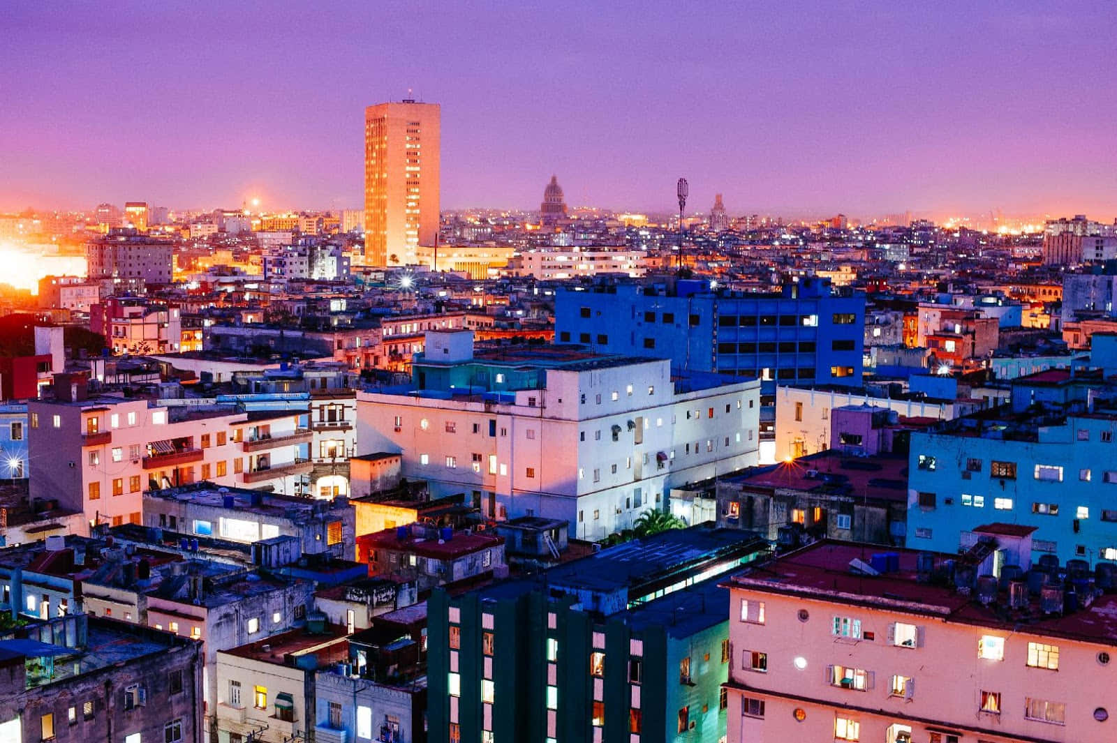 Cuba 桌布 壁紙 — 黃昏時分充滿活力的城市景觀，溫暖的燈光從窗戶照射出來，映襯著紫色和橙色的天空。