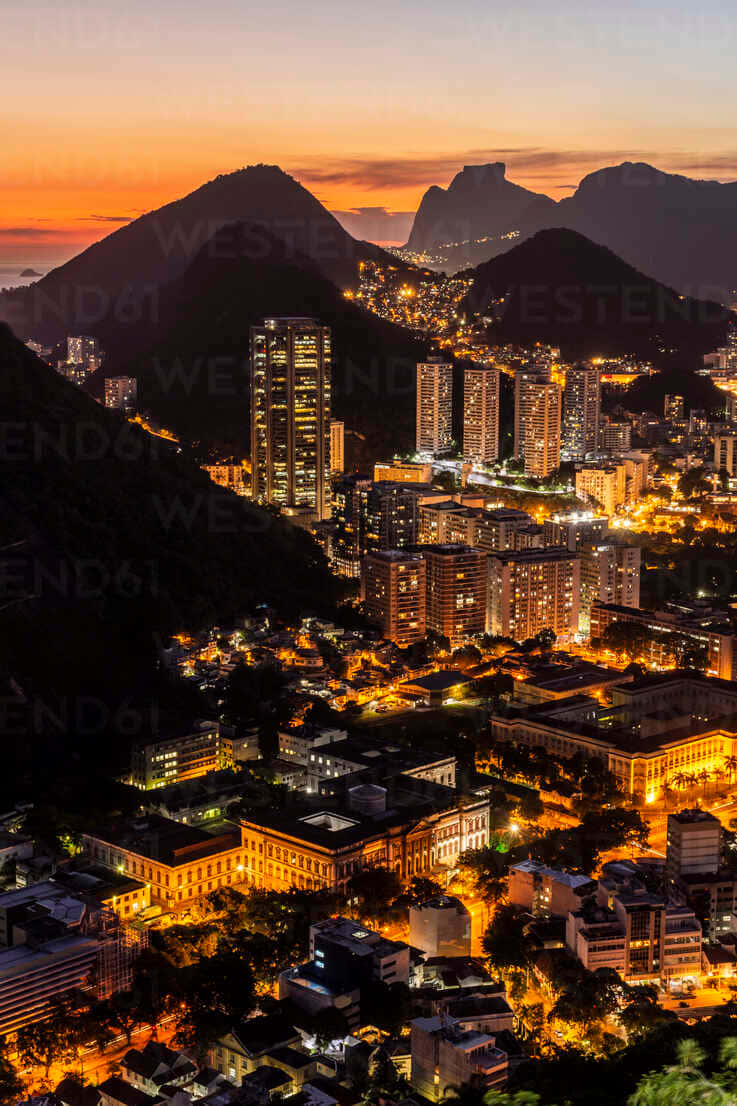 Beautiful Mountain 桌布 壁紙 — 黃昏時分充滿活力的城市景觀，發光的建築物坐落在黑暗的山脈之間，天空呈現橙色。