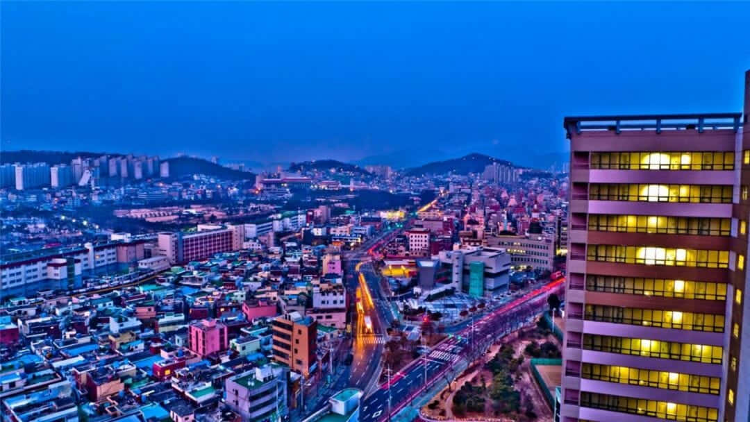 桌布 壁紙 — 黃昏時分充滿活力的城市景觀，閃爍的窗戶和流動的交通燈光映襯著深藍色的天空。