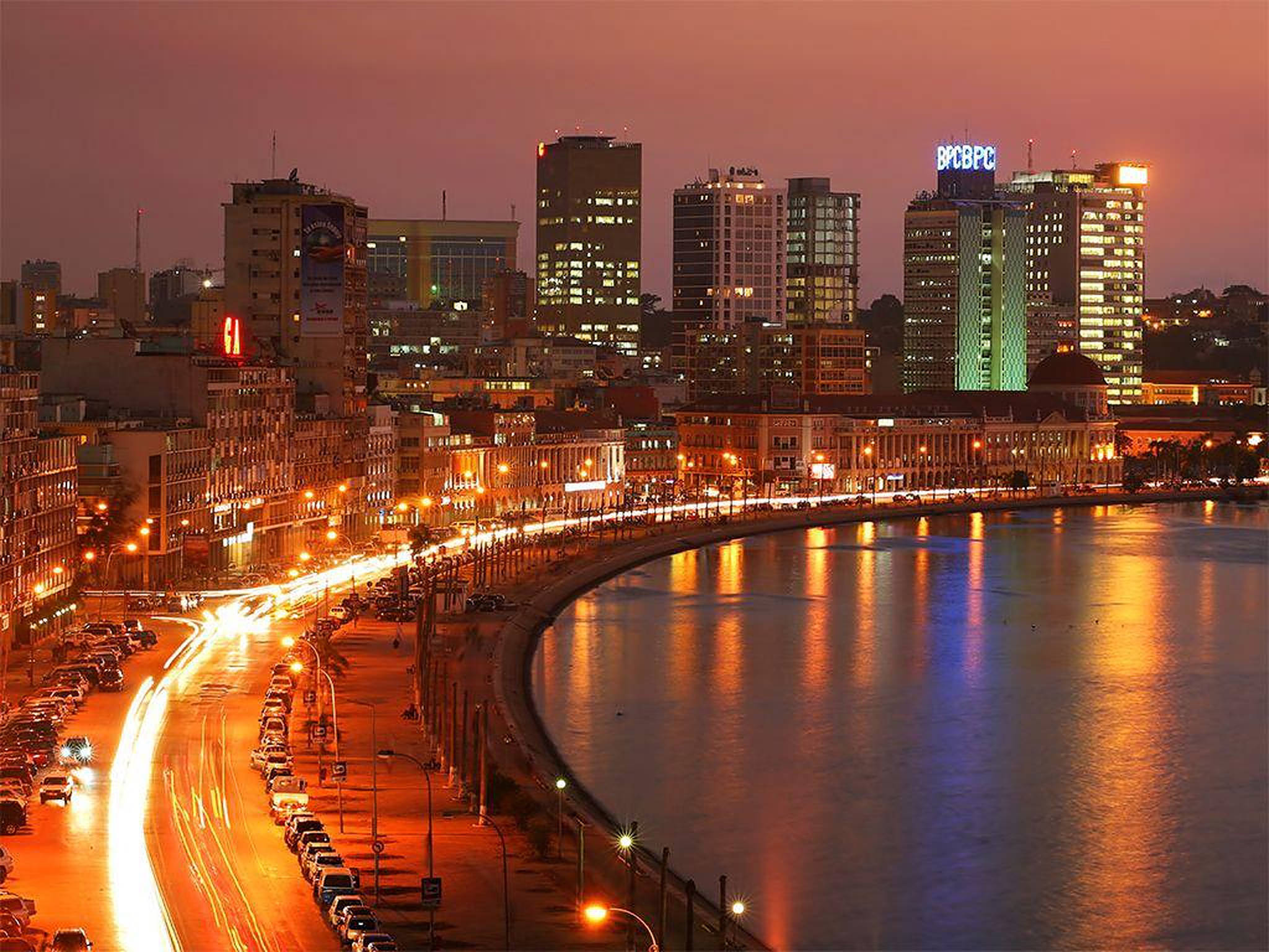 Angola 桌布 壁紙 — 黃昏時分充滿活力的城市景觀，閃爍的摩天大樓和海濱長廊上車流的燈光軌跡。