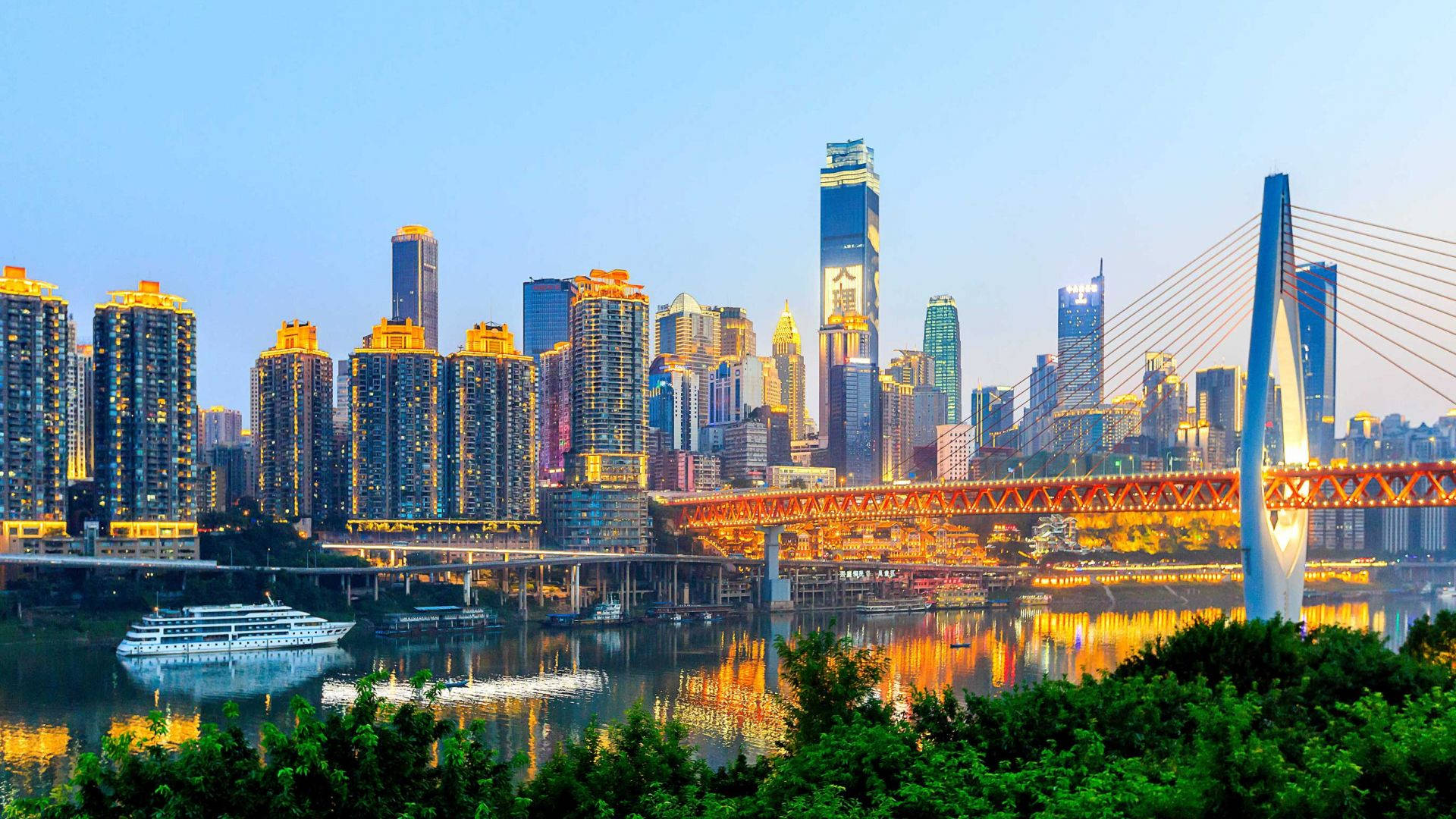 Chongqing 桌布 壁紙 — 黃昏時分充滿活力的城市景觀，閃爍的摩天大樓和一座紅色橋樑倒映在平靜的水面上。