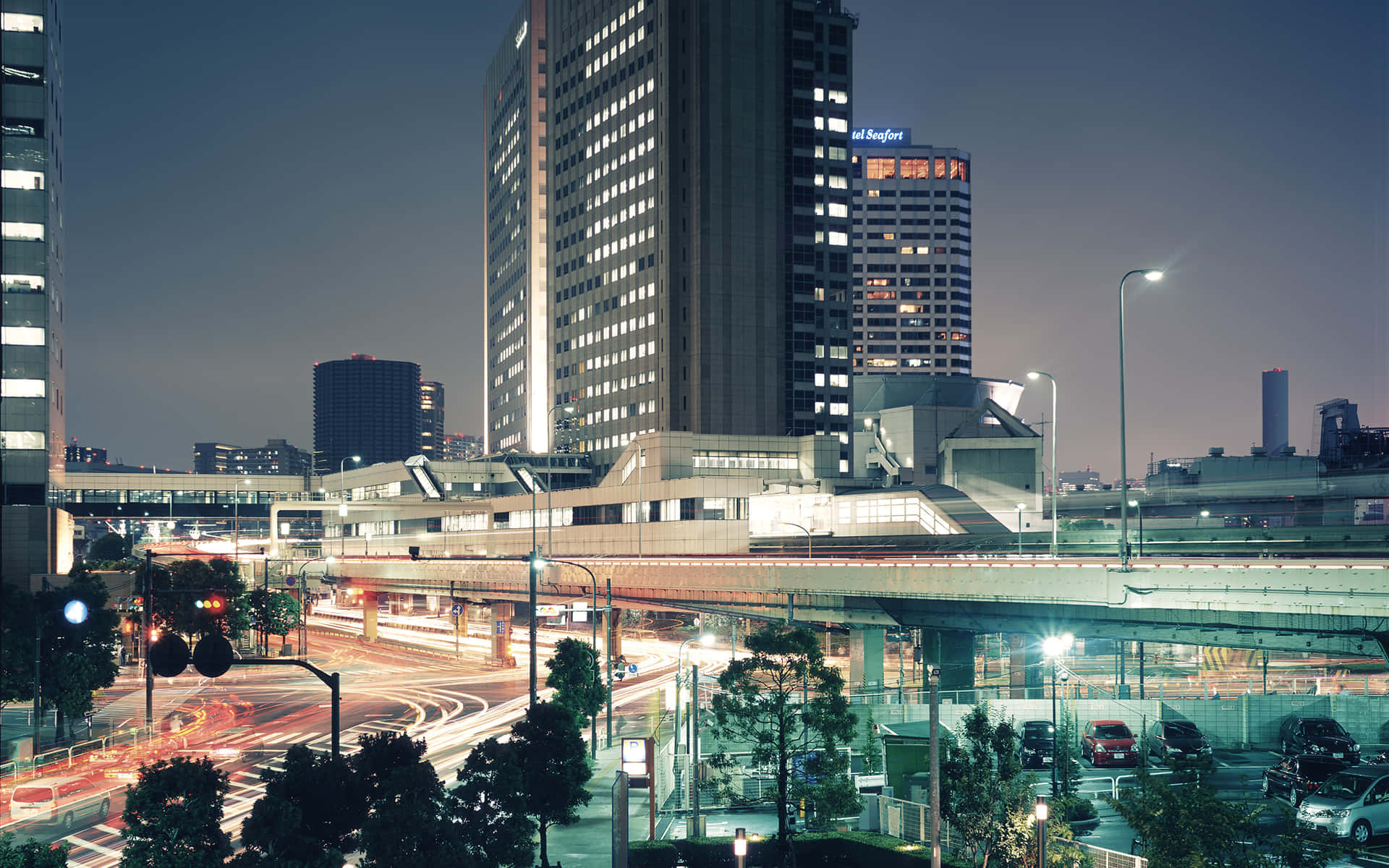 城市 桌布 壁紙 — 黃昏時分充滿活力的城市景觀，閃爍的摩天大樓和高架公路上汽車燈光的條紋。