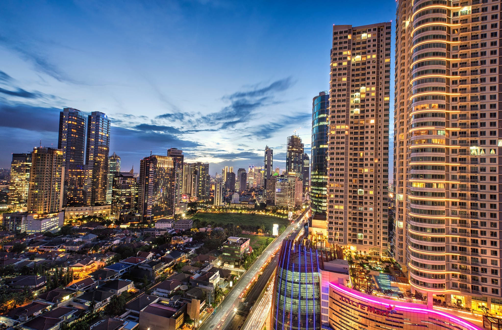 Jakarta 桌布 壁紙 — 黃昏時分充滿活力的城市景觀，高聳的摩天大樓在深藍色雲彩斑斕的天空中閃耀。