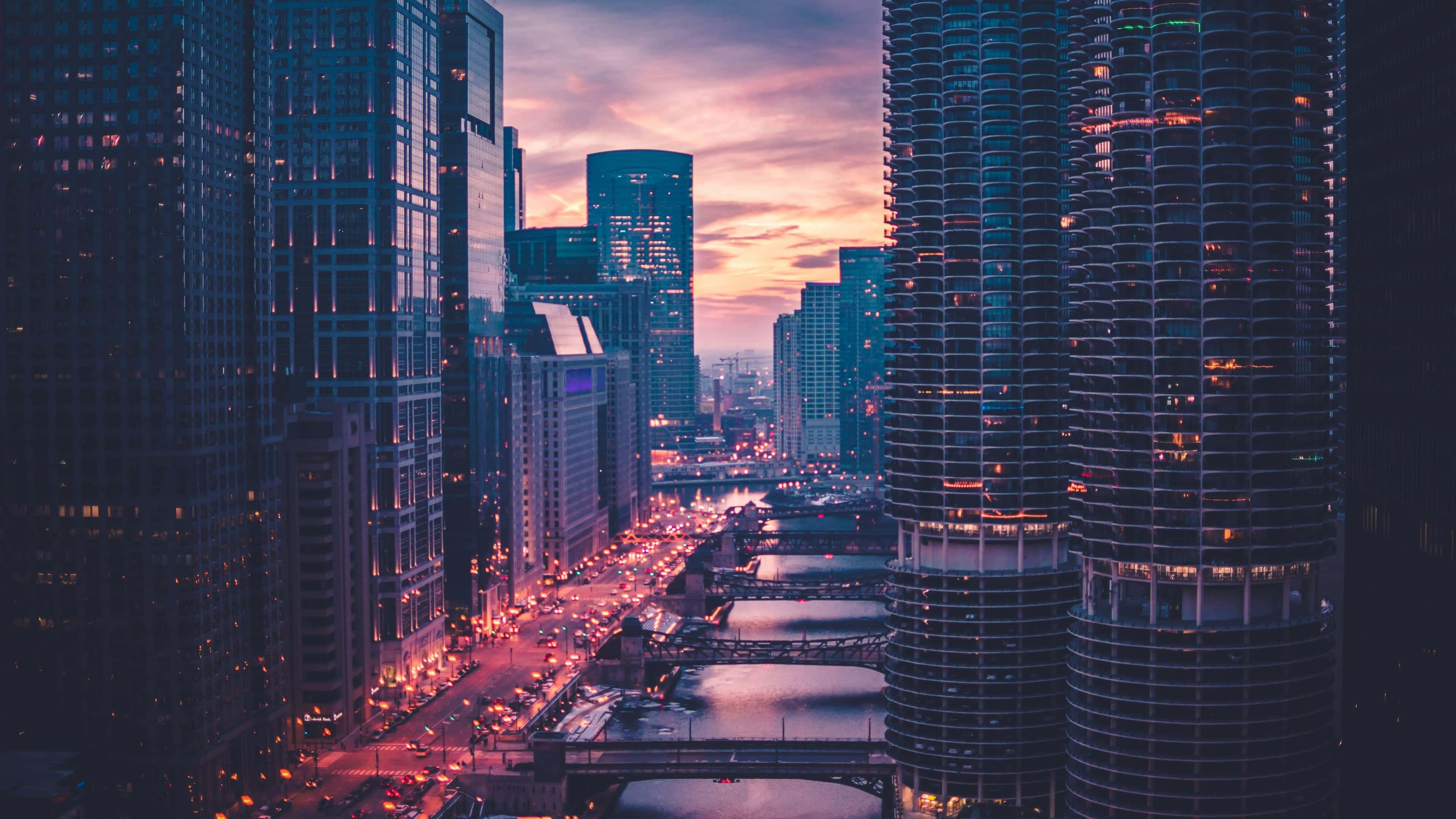 美國 桌布 壁紙 — 黃昏時分充滿活力的城市景觀，高聳的摩天大樓在繁忙的河流和橋樑上反射出粉紅色和橙色的天空。