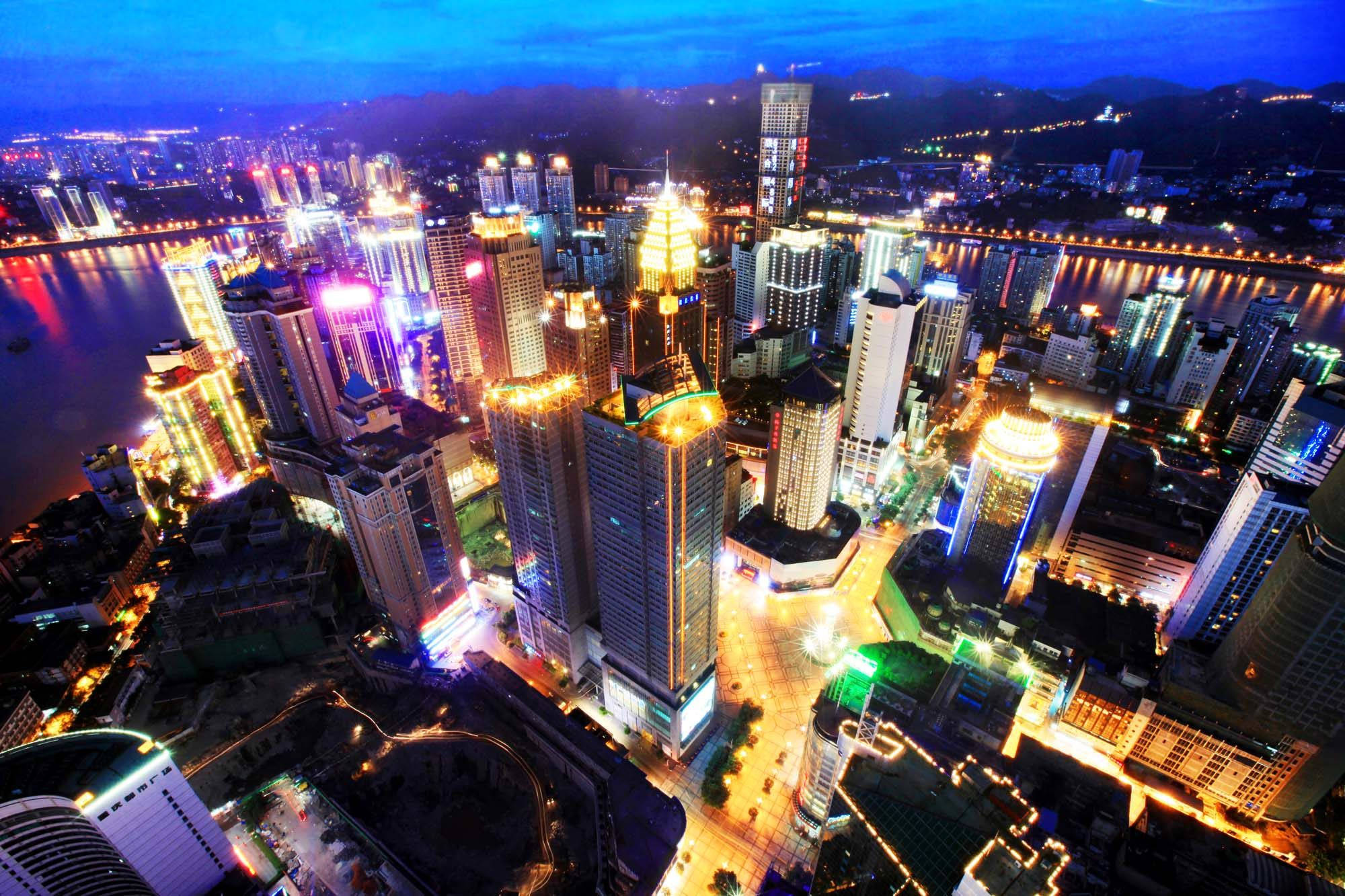 Chongqing 桌布 壁紙 — 黃昏時分充滿活力的城市景觀鳥瞰圖，霓虹燈照亮的摩天大樓倒映在河面上。