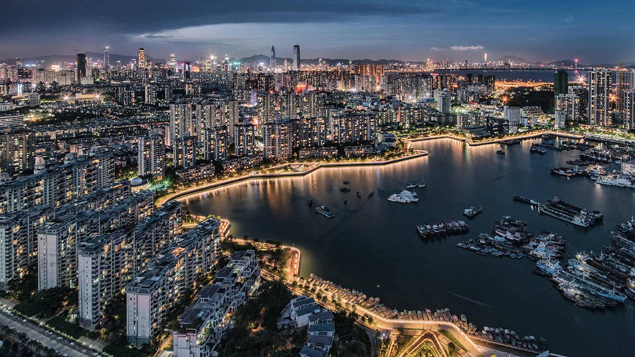 Shenzhen 桌布 壁紙 — 黃昏時分充滿活力的城市景觀鳥瞰圖，閃爍的摩天大樓和船隻停泊在蜿蜒的海濱。