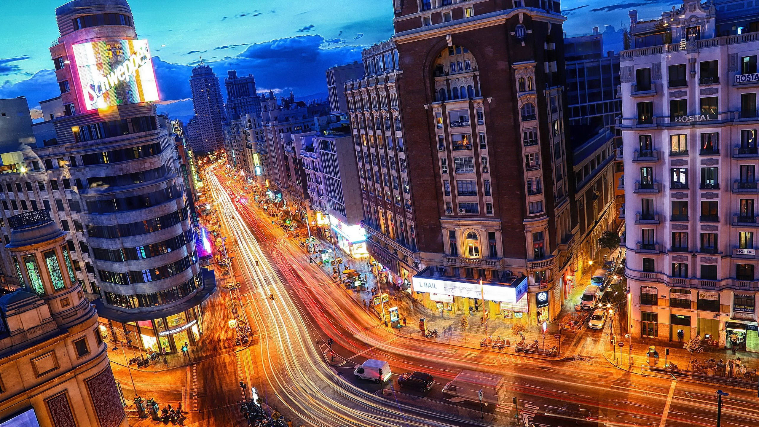Madrid 桌布 壁紙 — 黃昏時分充滿活力的城市街道，交通燈光和照亮建築物在深藍色天空下閃耀。