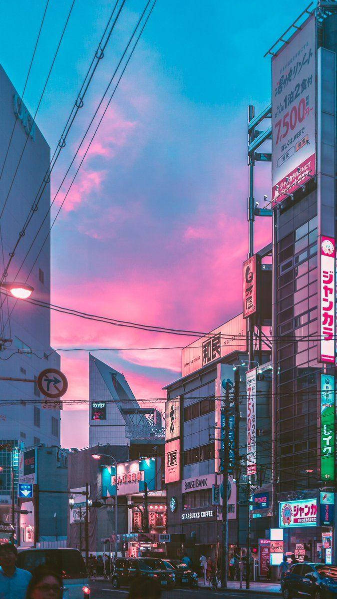 日本 桌布 壁紙 — 黃昏時分充滿活力的城市街道，粉紅色和藍色的天空映照著發光的霓虹燈招牌和擁擠的人行道。
