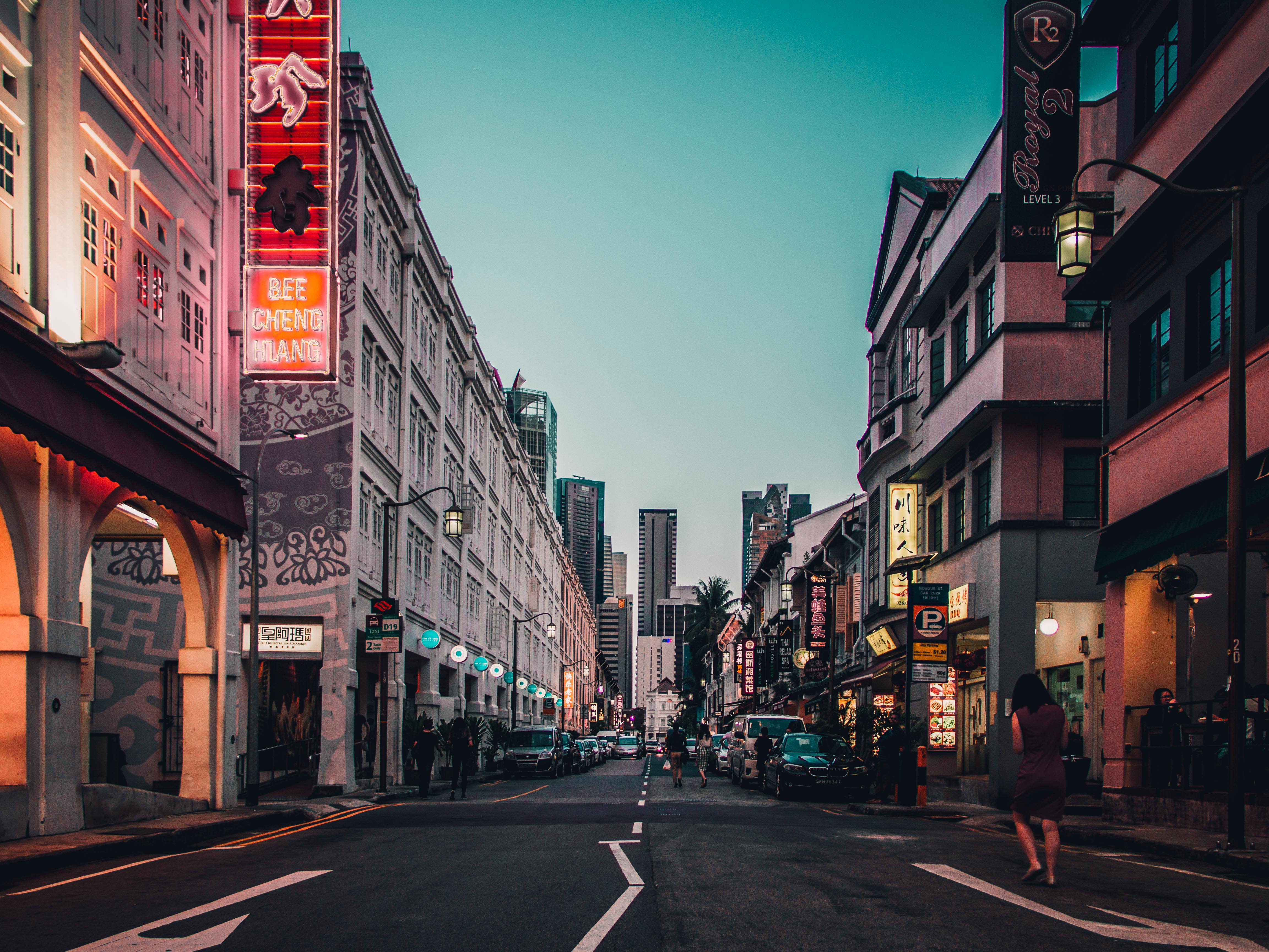 Singapore 桌布 壁紙 — 黃昏時分充滿活力的城市街道，閃爍的霓虹燈招牌和殖民風格建築框住了通往現代摩天大樓的景色。