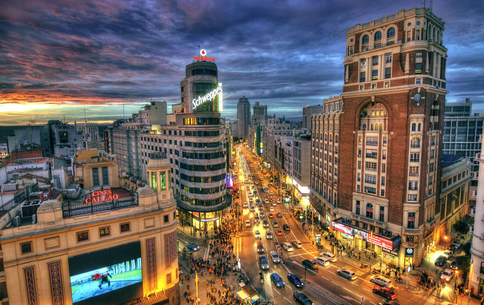 Madrid 桌布 壁紙 — 黃昏時分充滿活力的城市街道，霓虹燈閃爍，交通繁忙，天空色彩繽紛，充滿戲劇性。