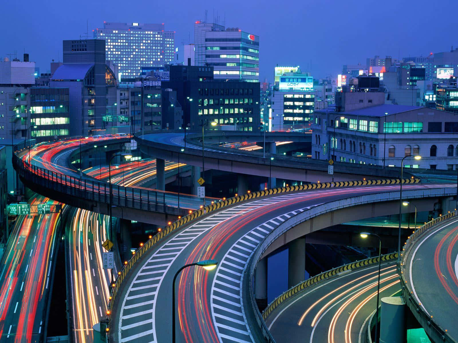 Beautiful Place 桌布 壁紙 — 黃昏時分充滿活力的城市高速公路交匯處，以燈火通明的城市摩天大樓為背景，車流留下紅色和白色的光跡。