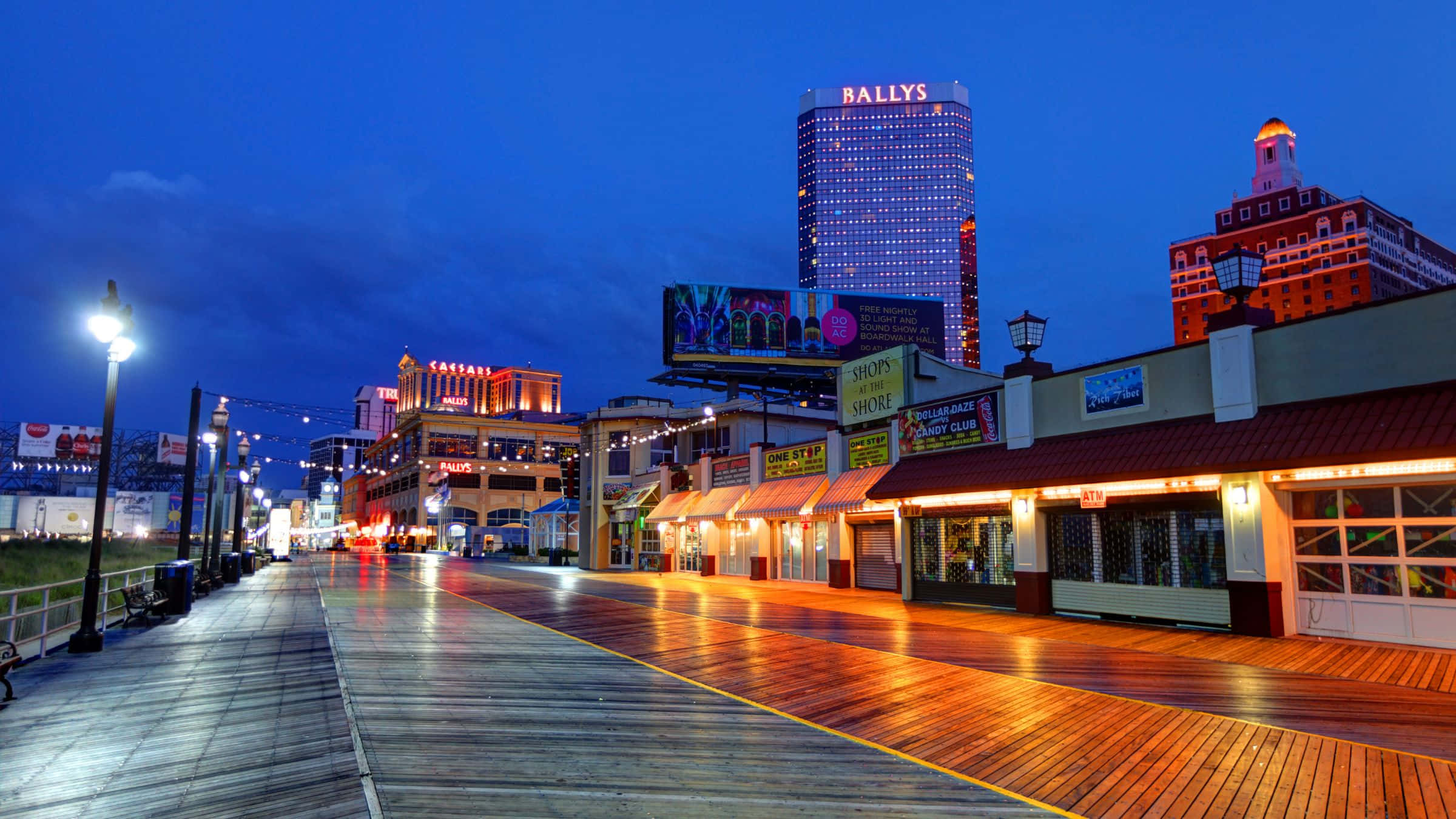 德州 桌布 壁紙 — 黃昏時分充滿活力的木板路，霓虹燈閃爍，濕潤的木板上反射著城市燈光，深藍色的天空下。