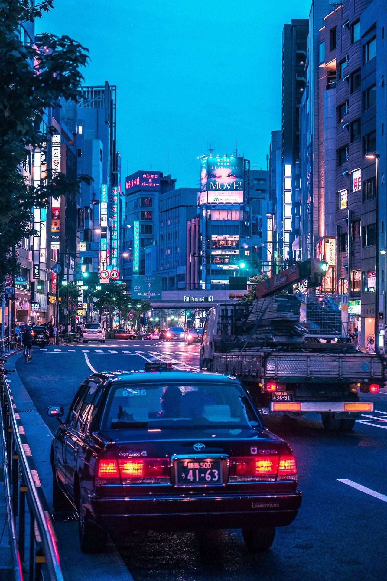 東京 桌布 壁紙 — 黃昏時分充滿活力的東京街道，發光的霓虹燈招牌映照在潮濕的路面上，汽車穿梭於繁忙的城市峽谷中。