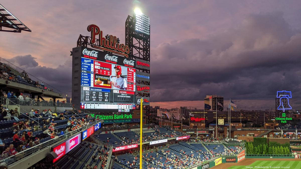 Phillies 桌布 壁紙 — 黃昏時分充滿活力的棒球場，巨大的記分板顯示比賽數據，發光的 Phillies 標誌映襯著戲劇性的紫色天空。