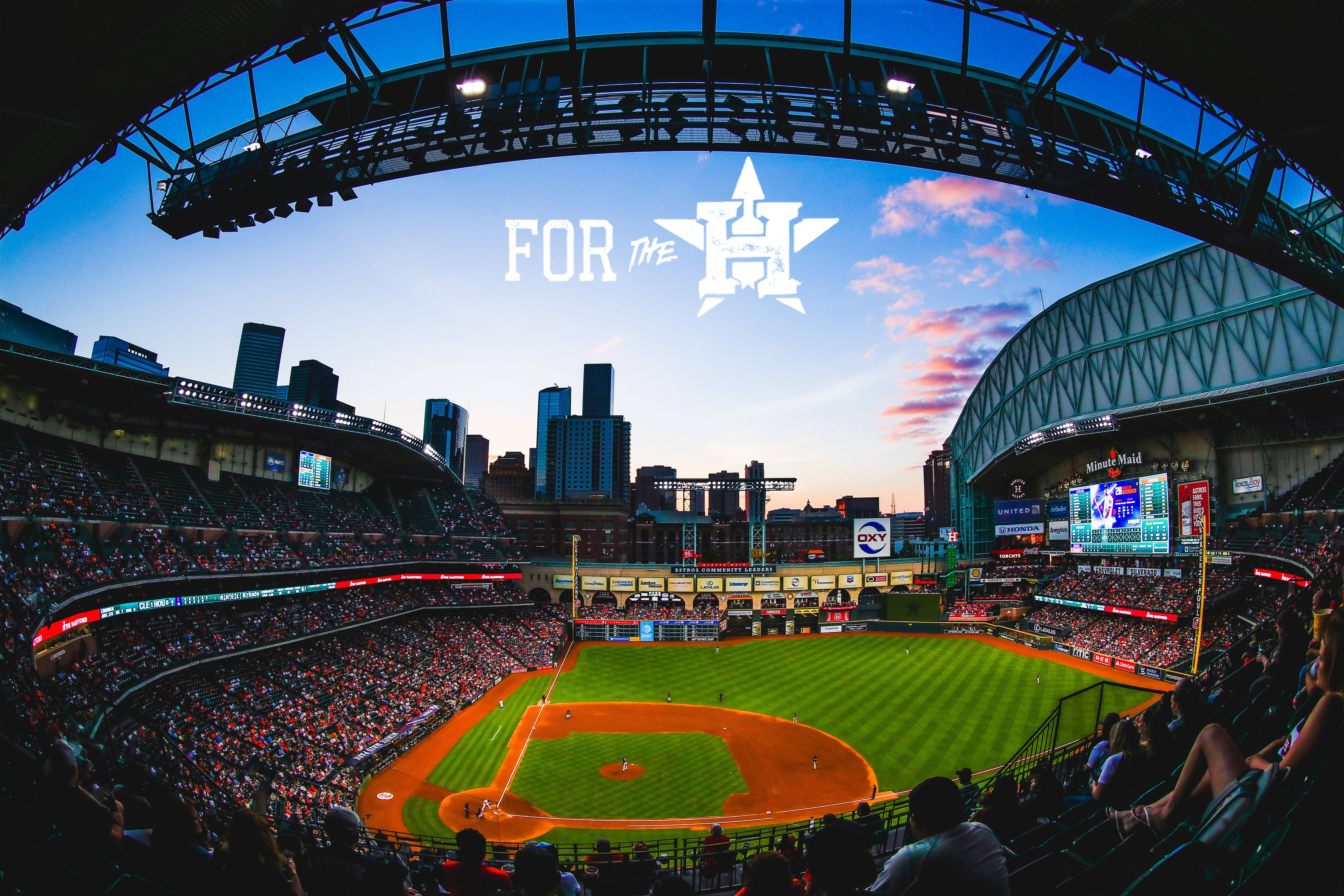 Astros 桌布 壁紙 — 黃昏時分充滿活力的棒球場，球迷坐滿座位，城市天際線在球場後方閃耀。