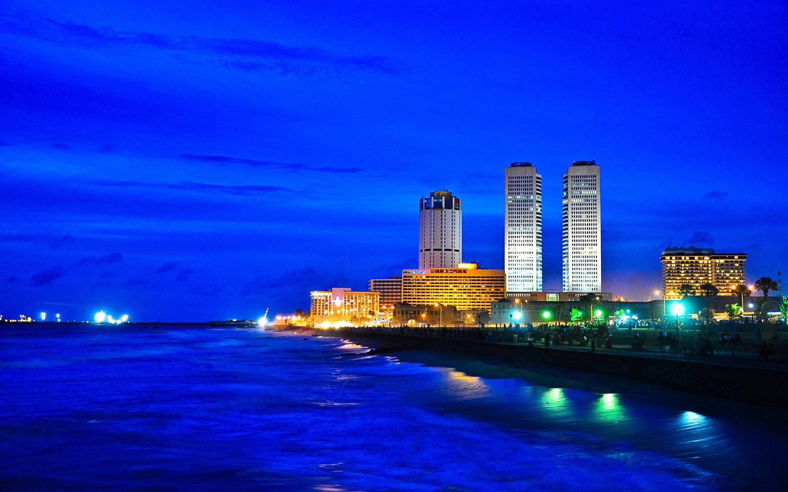 Sri Lanka 桌布 壁紙 — 黃昏時分充滿活力的海岸城市景觀，閃爍的摩天大樓倒映在深藍色的海浪上。