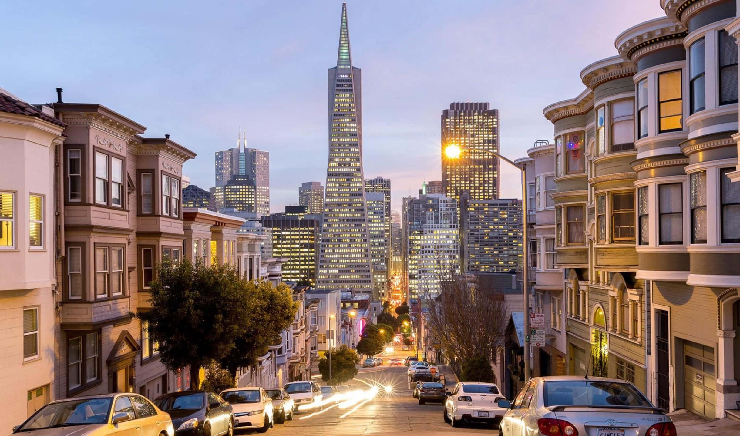 2440x1440 San Francisco 桌布 壁紙 — 黃昏時分充滿活力的舊金山街道，歷史悠久的維多利亞式房屋排列在通往發光的泛美金字塔和城市天際線的道路兩旁。