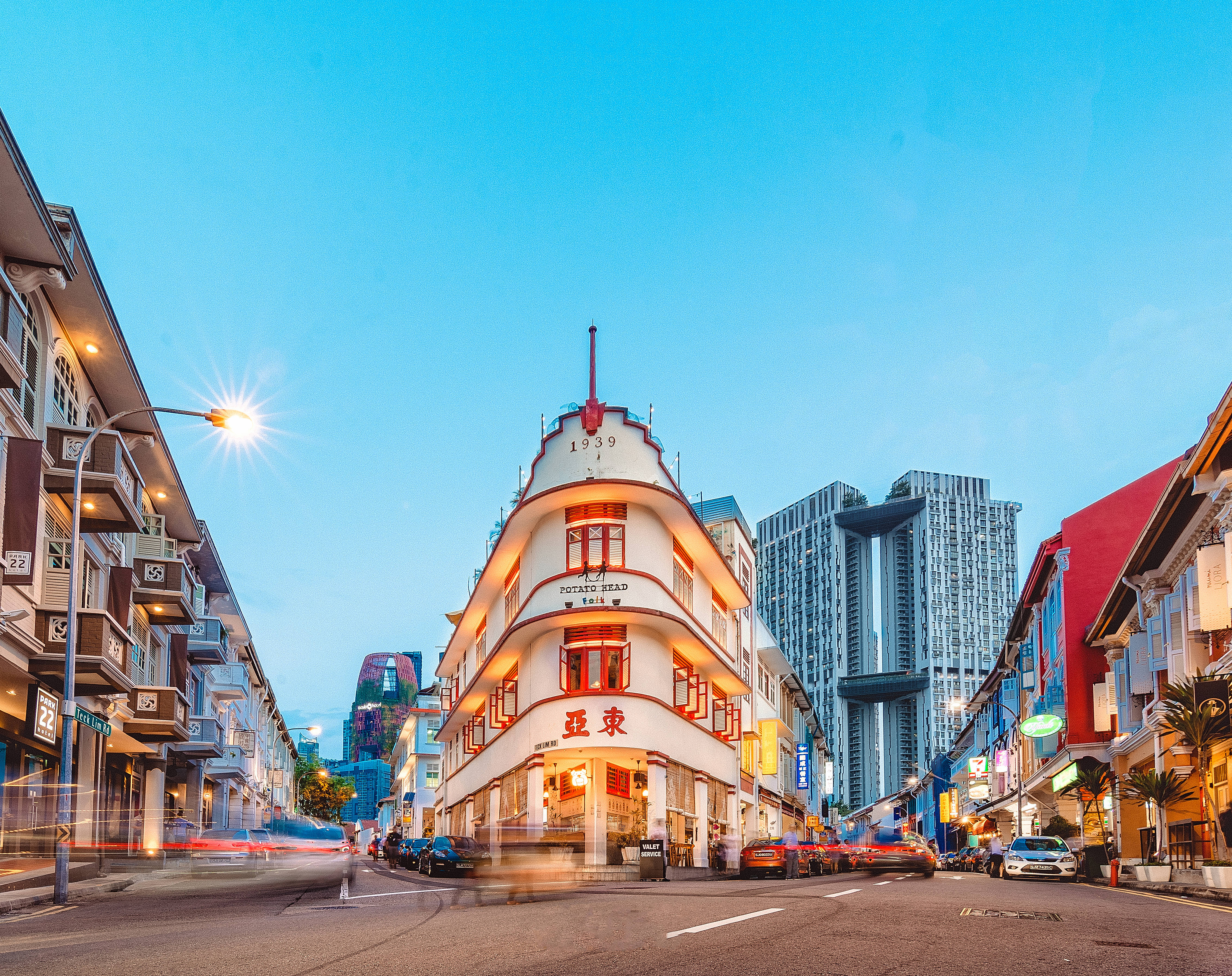 Singapore 桌布 壁紙 — 黃昏時分充滿活力的街景，一座歷史悠久的白色裝飾藝術建築在晴朗的藍天下溫暖地發光。