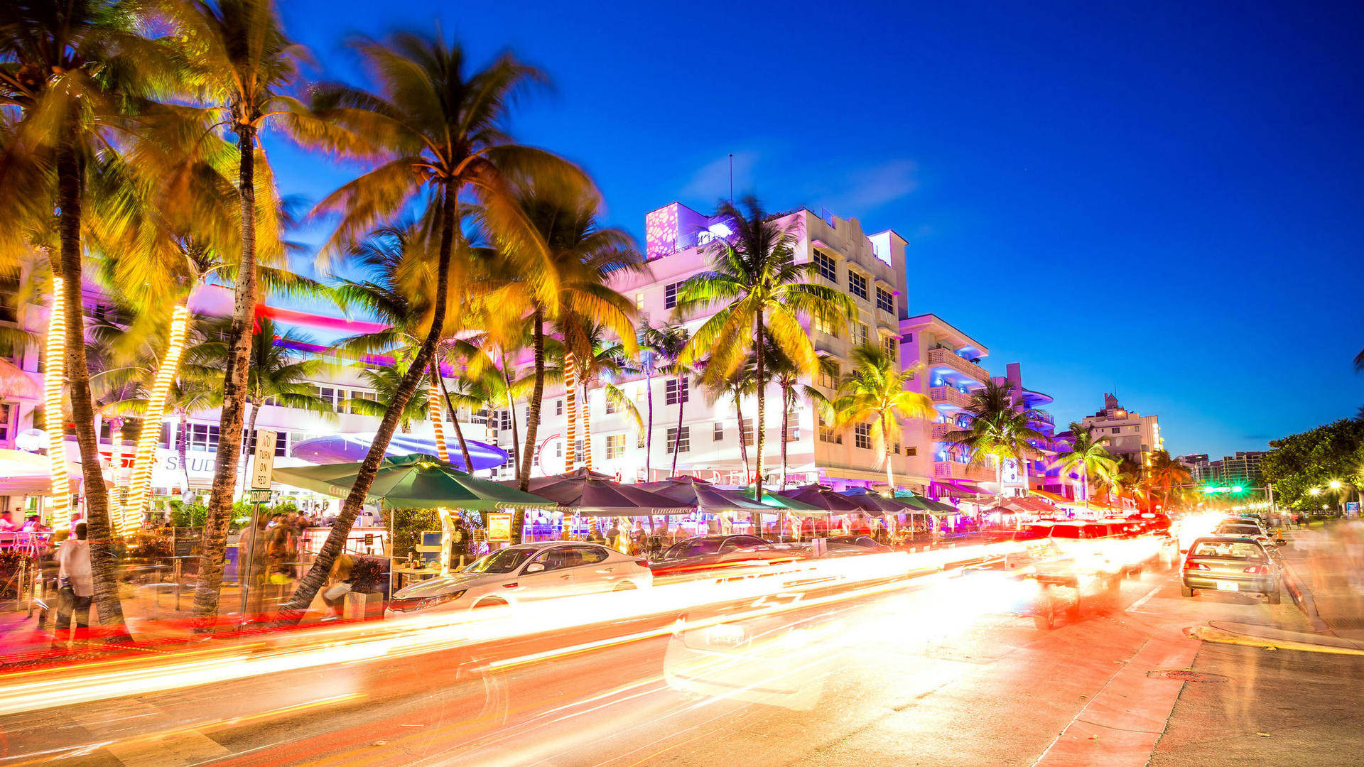 Miami 桌布 壁紙 — 黃昏時分充滿活力的邁阿密海灘街道，棕櫚樹在霓虹燈和汽車燈光拖影下閃耀。