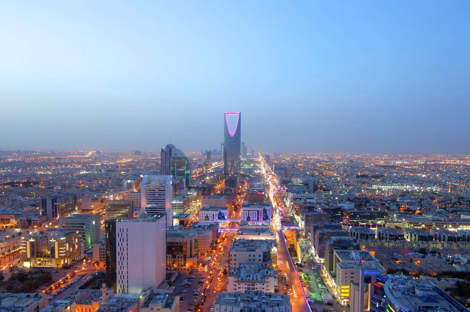 Riyadh 桌布 壁紙 — 黃昏時分利雅德城市景觀的鳥瞰圖，街道閃爍，王國塔被紫色照亮。