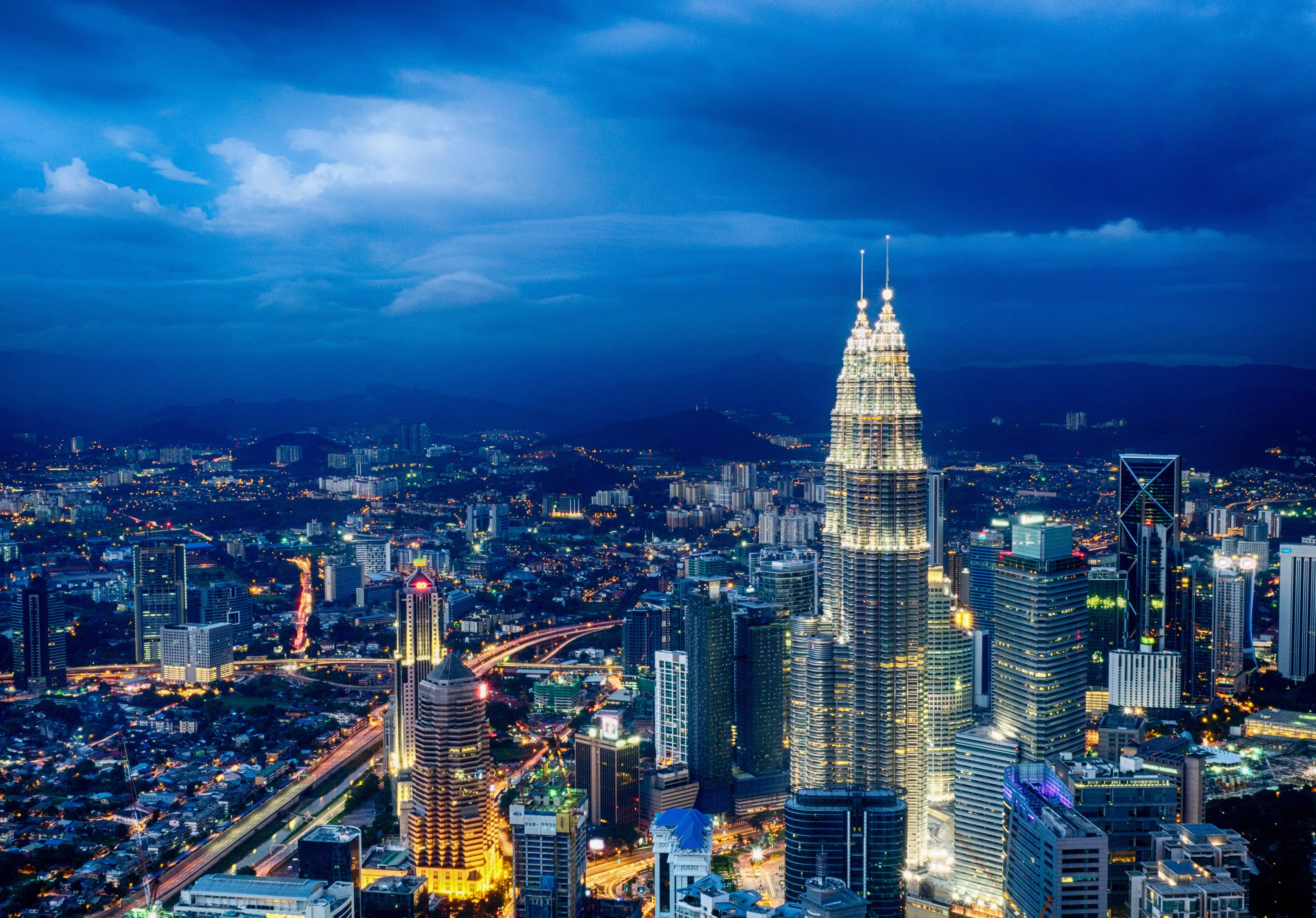 Malaysia 桌布 壁紙 — 黃昏時分吉隆坡天際線的鳥瞰圖，亮燈的雙子星塔和城市燈光在憂鬱的藍天下蔓延。